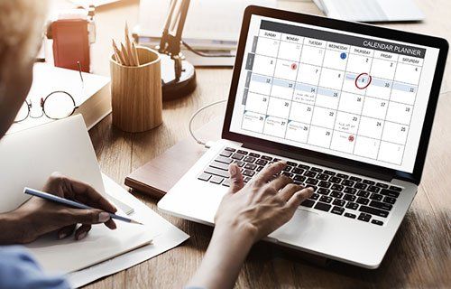 A person is using a laptop computer with a calendar on the screen.