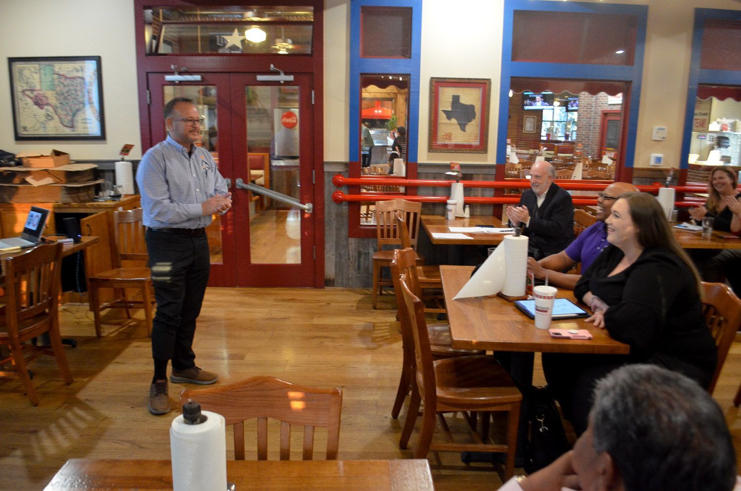 A man is standing in front of a group of people sitting at tables in a restaurant
