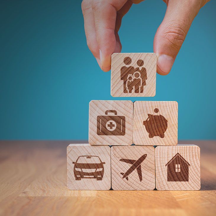 Hand placing a family icon block on a stack of insurance-related blocks: car, travel, home, health, and savings.