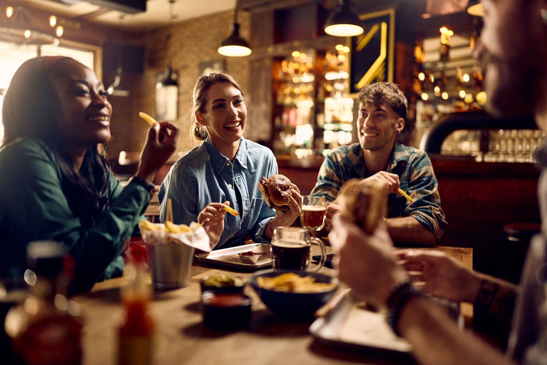 A multiracial group of happy friends eating burgers while drinking beer in a pub.