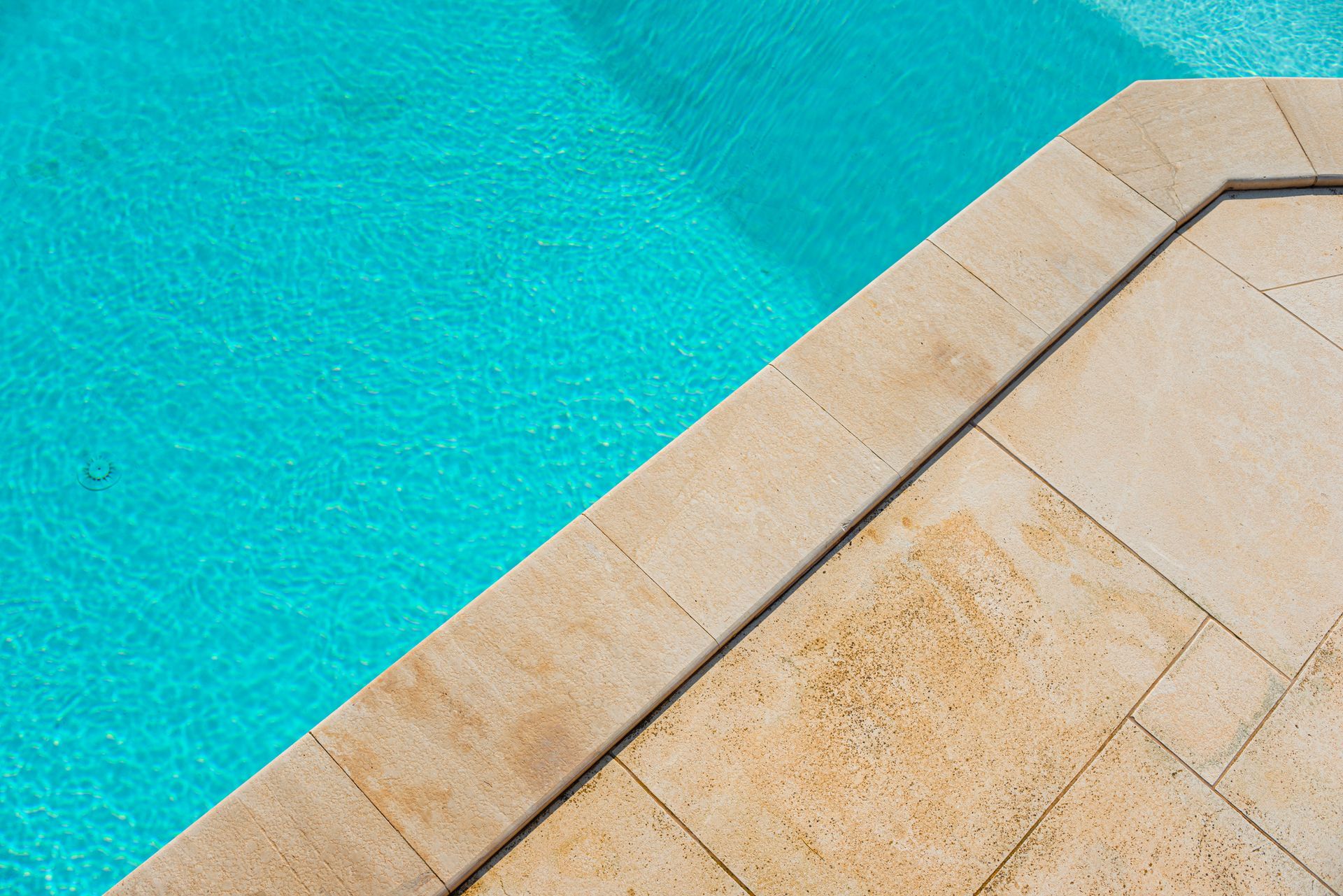 Clean pool water beside light stone pool deck with clear blue surface for pool maintenance visuals.