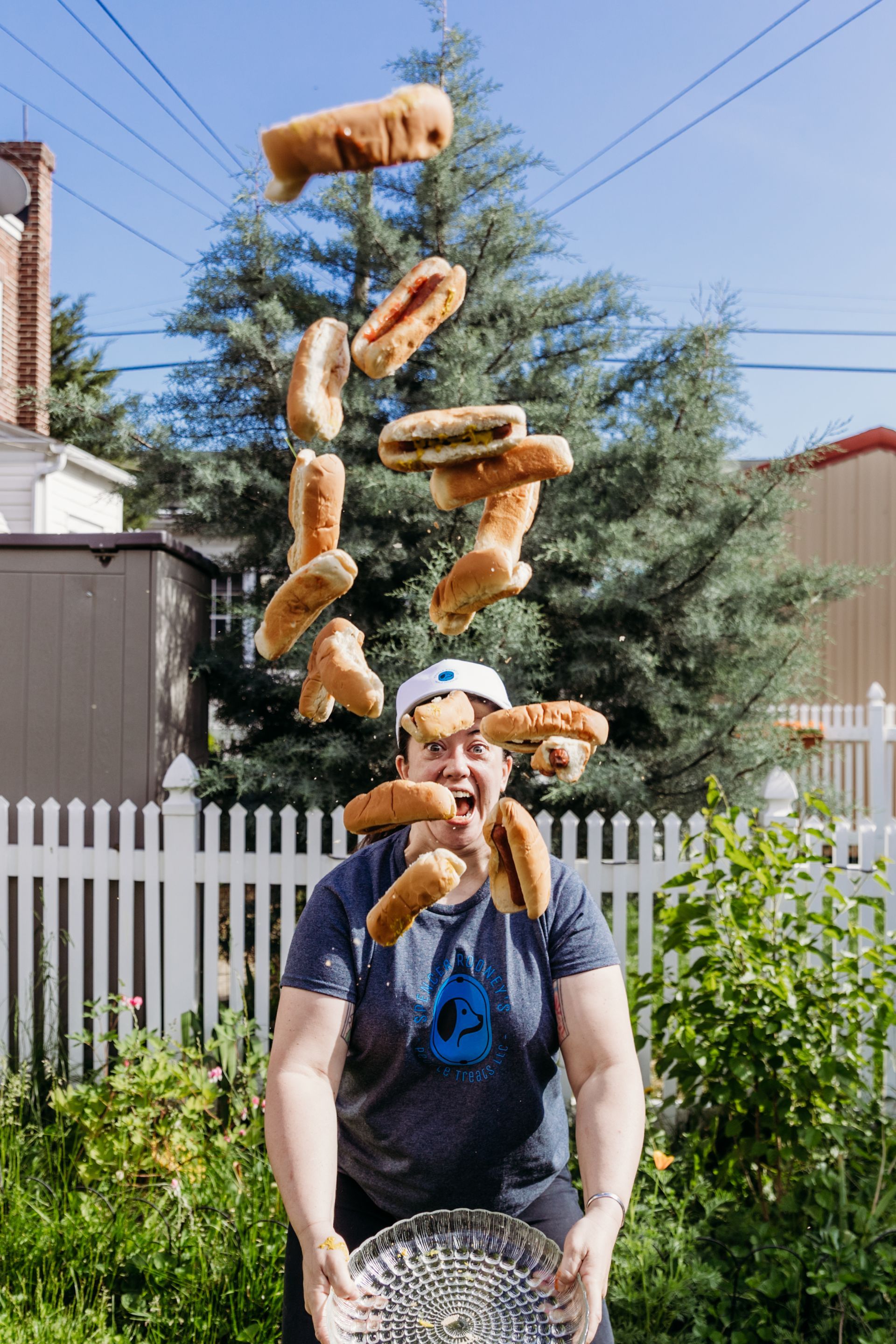 Woman is throwing hot dogs in the air while holding a bowl.
