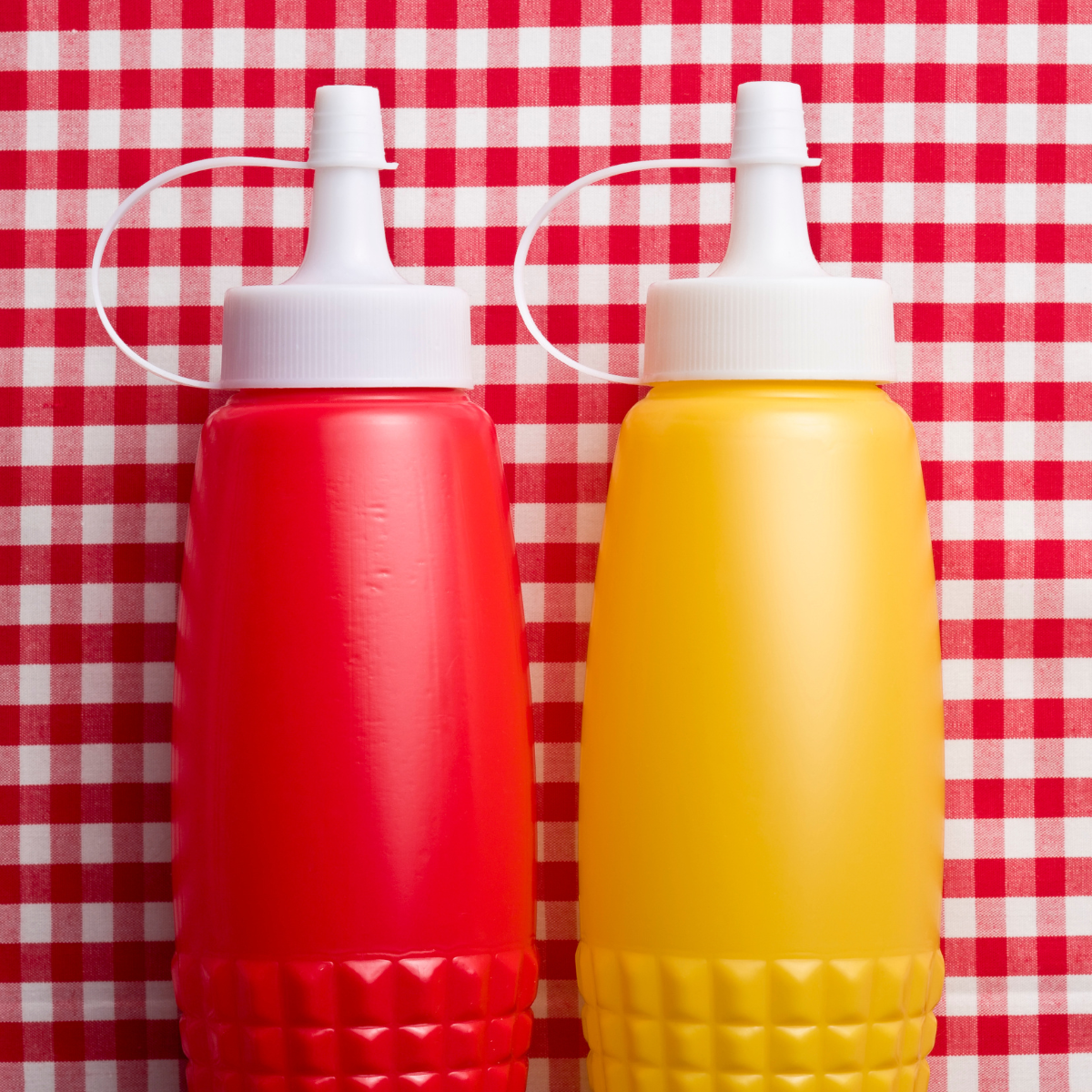 Two bottles of ketchup and mustard on a checkered table cloth