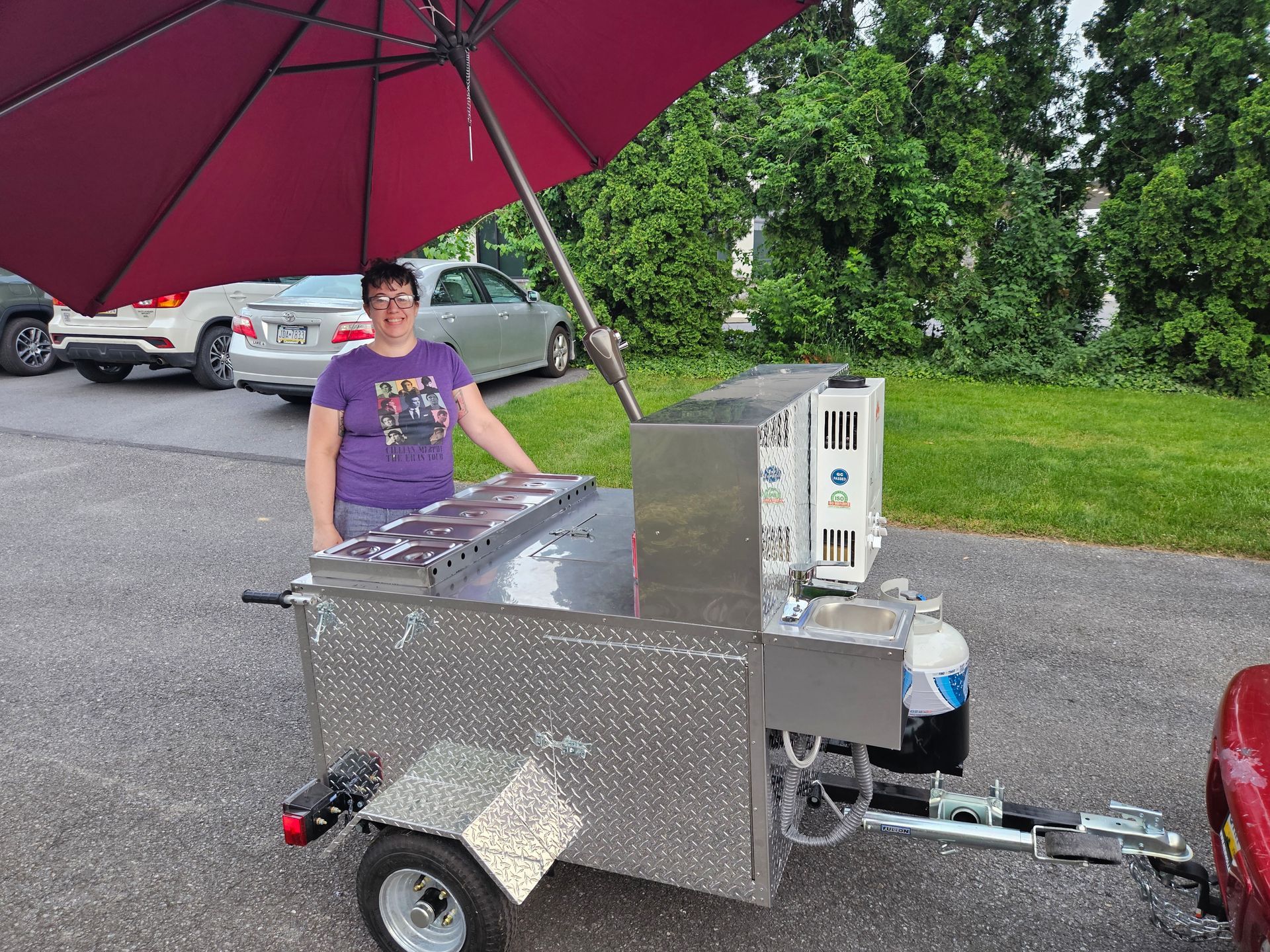 A woman is standing next to a trailer with a red umbrella.