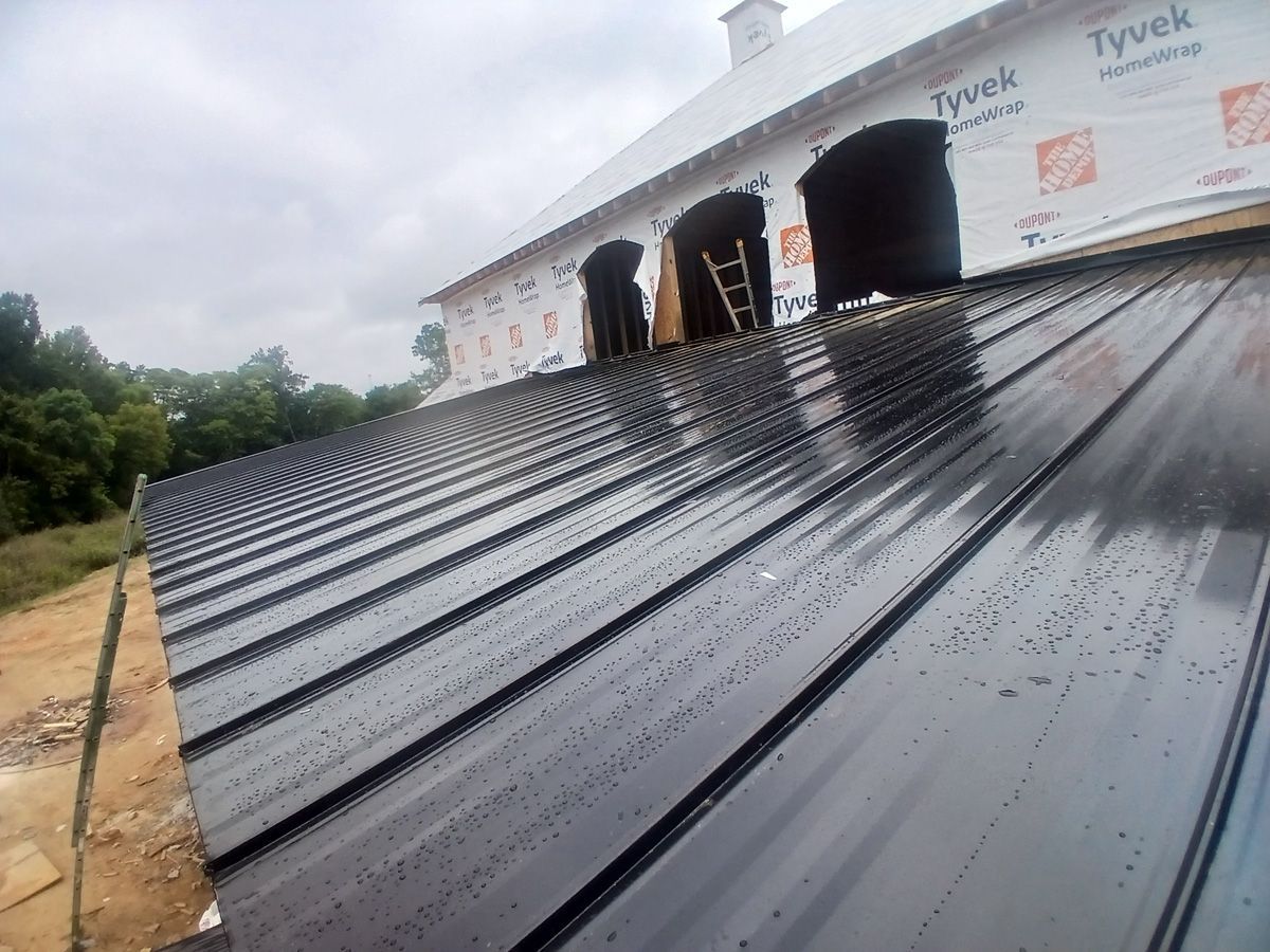 Black metal roof with three vents and building wrap under an overcast sky.