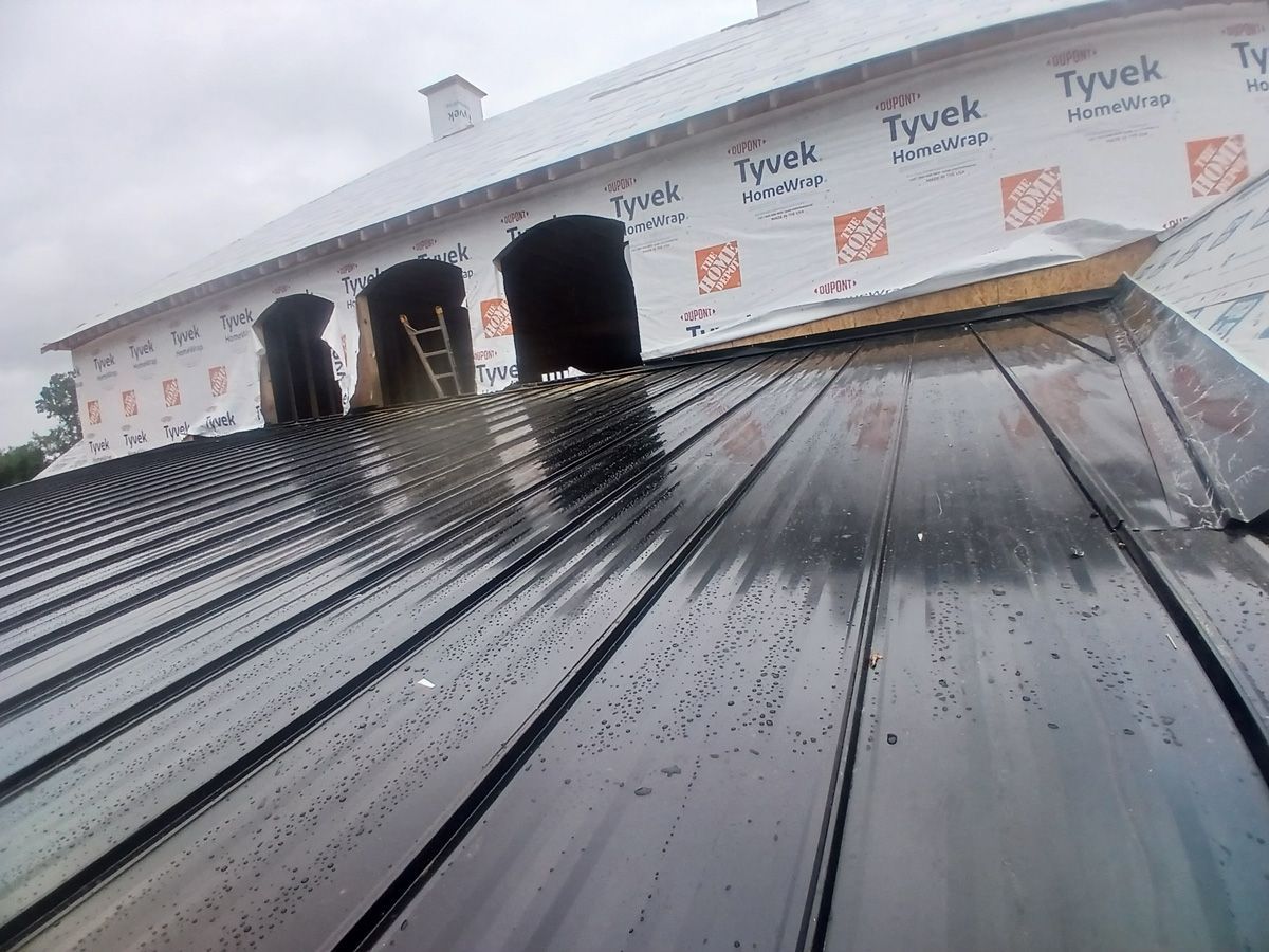 Dark metal roof partially installed on a building under construction; cloudy sky.