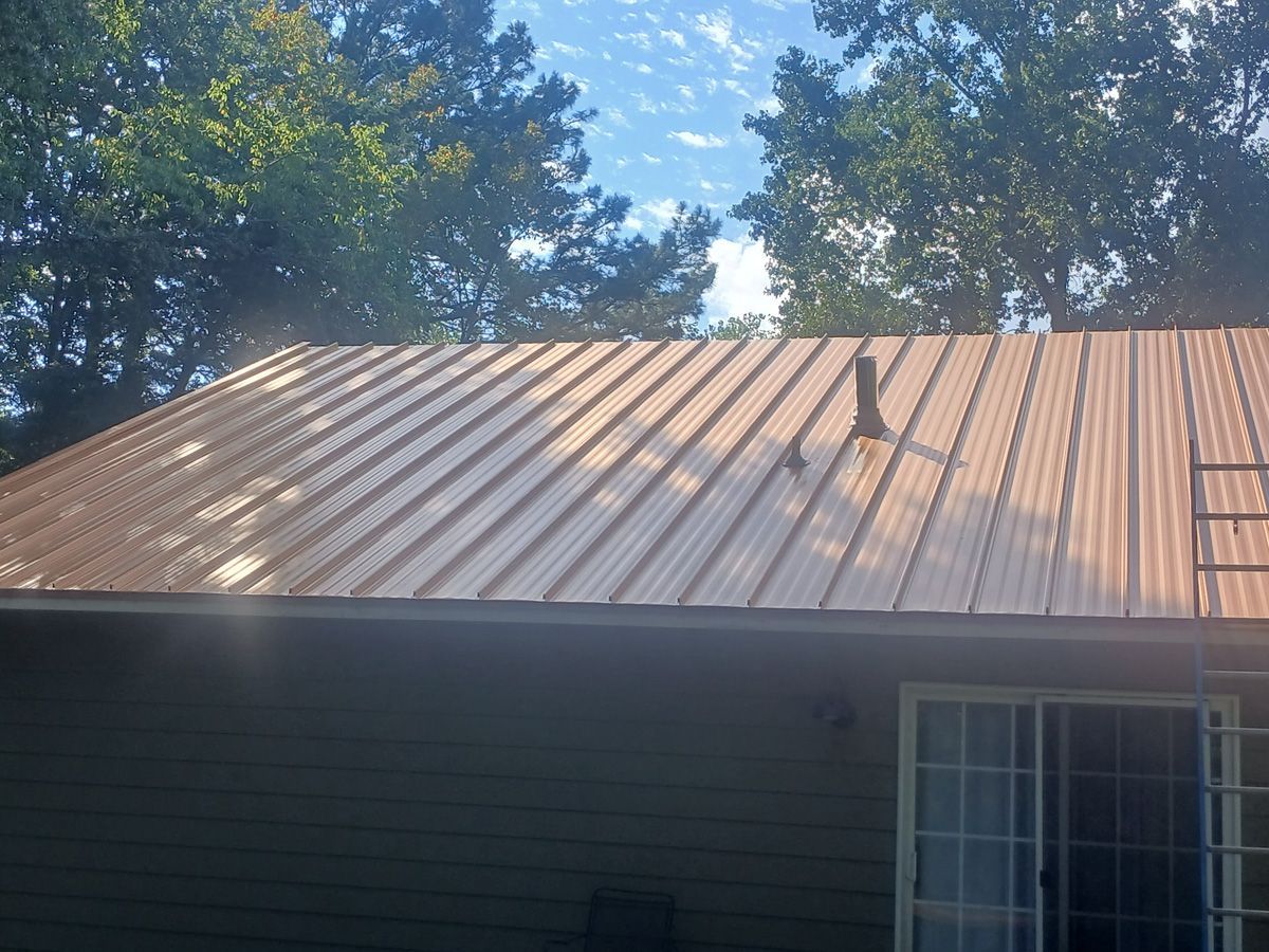 Brown metal roof on a house against a backdrop of trees and a partly cloudy sky.