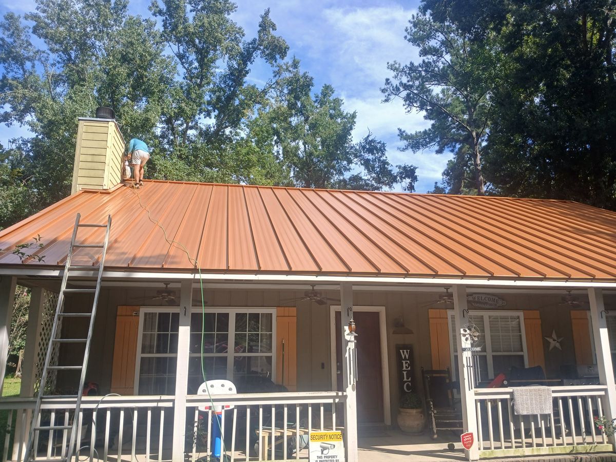 Tan house with metal roof; person on roof near chimney, ladder in view.