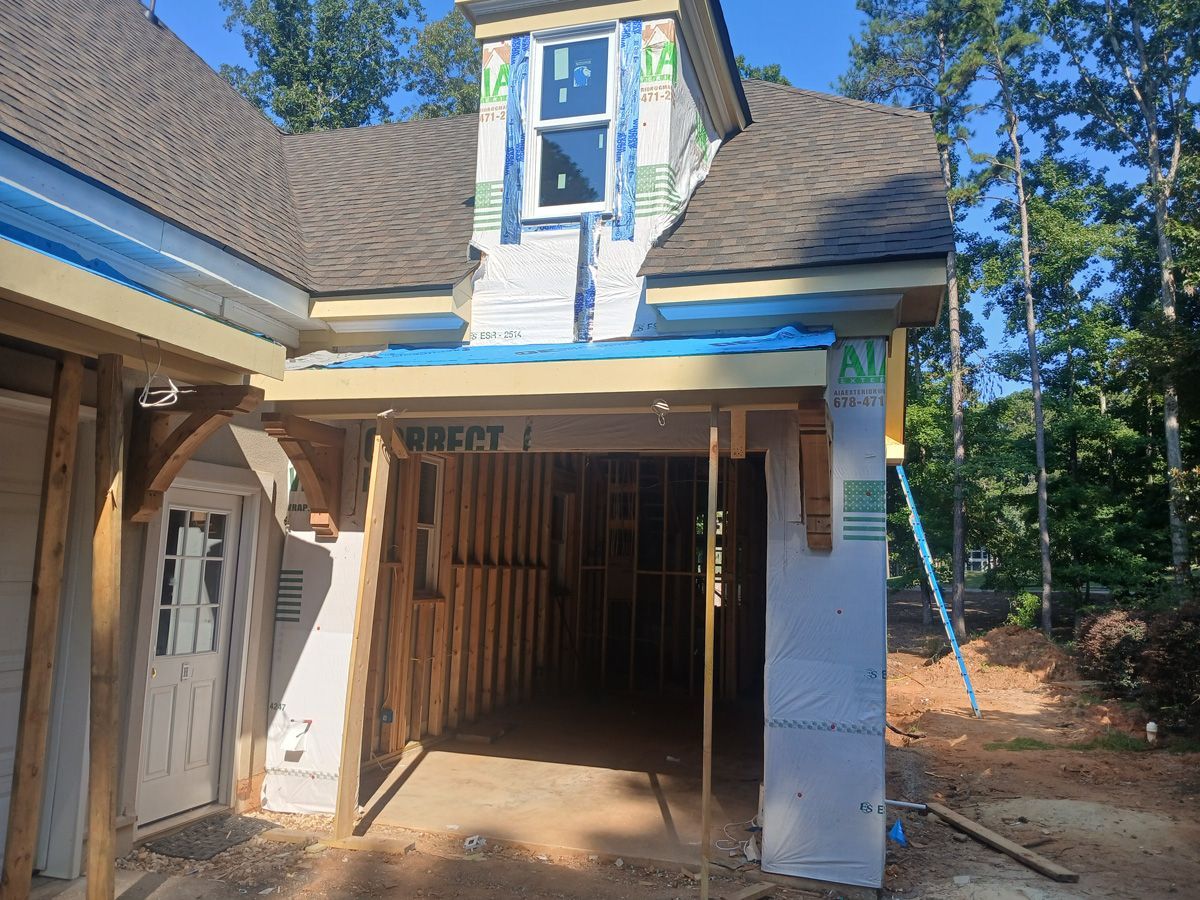 Construction of a house, exterior view. Garage entrance with wooden framing and partially finished walls. Blue tarp and unfinished roof.