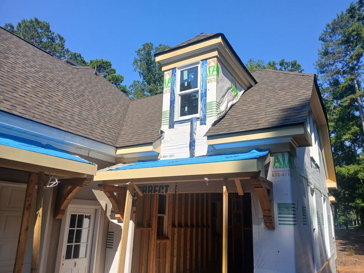 A partially constructed house with a dormer window and blue tarps, under a sunny sky.