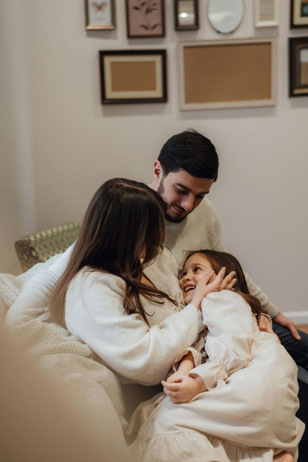 Family cuddling on a beige couch in a cozy living room, smiling and embracing a baby.