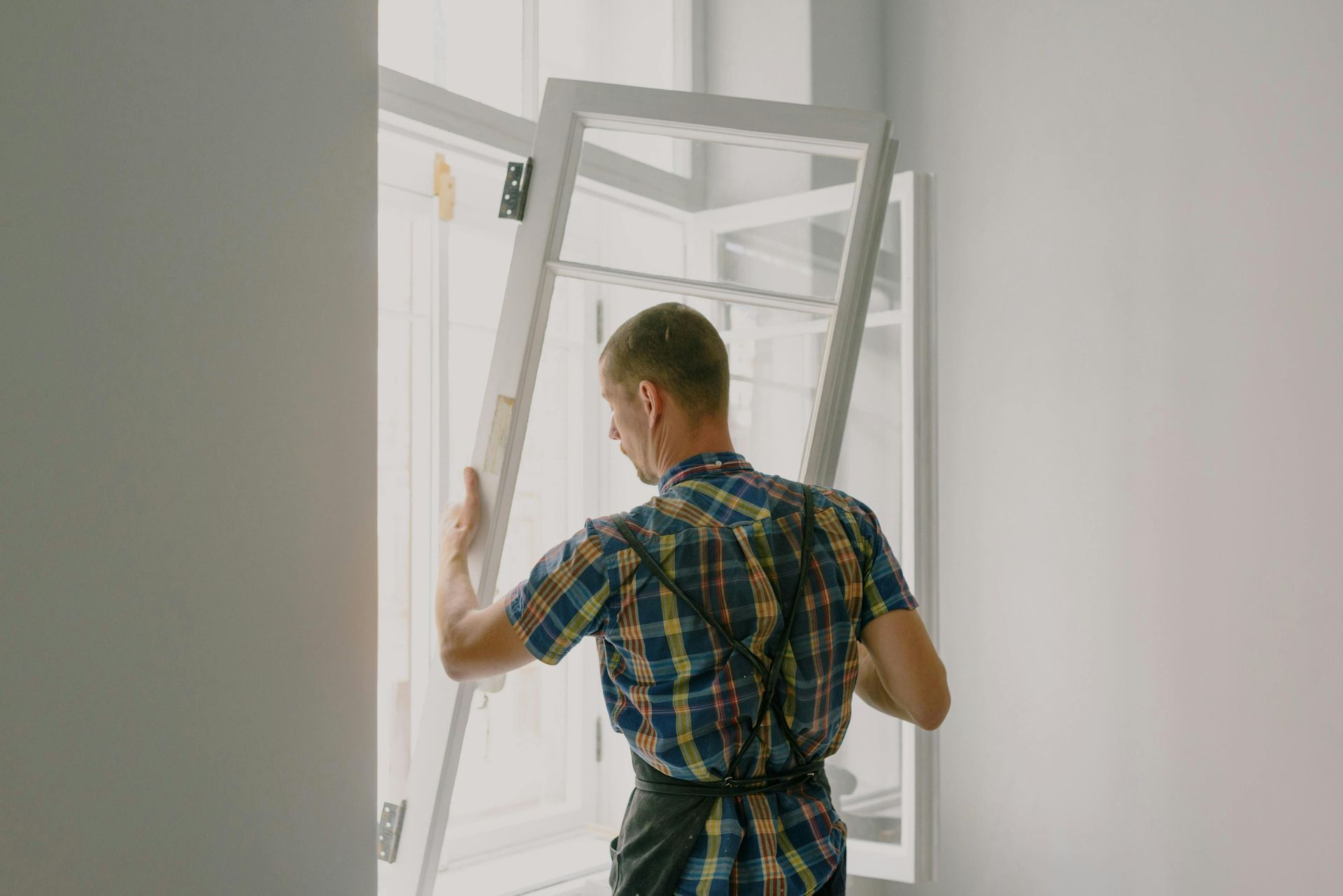Man installing a window frame in a bright room, holding a white frame open.