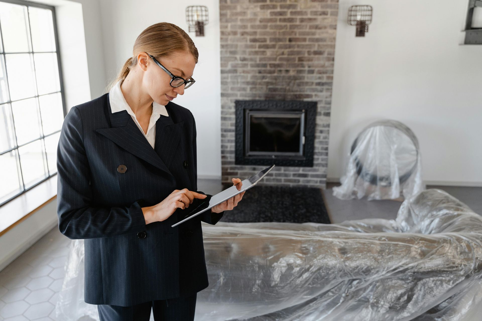 Person using a tablet in a newly renovated room with a fireplace, furniture covered in plastic