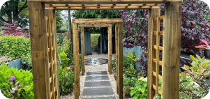 Wooden arbor walkway through a garden, stone path, lush greenery.