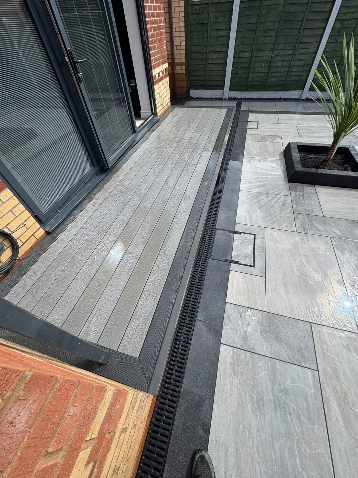 Composite decking leads to a patio with a drainage system and potted plant.