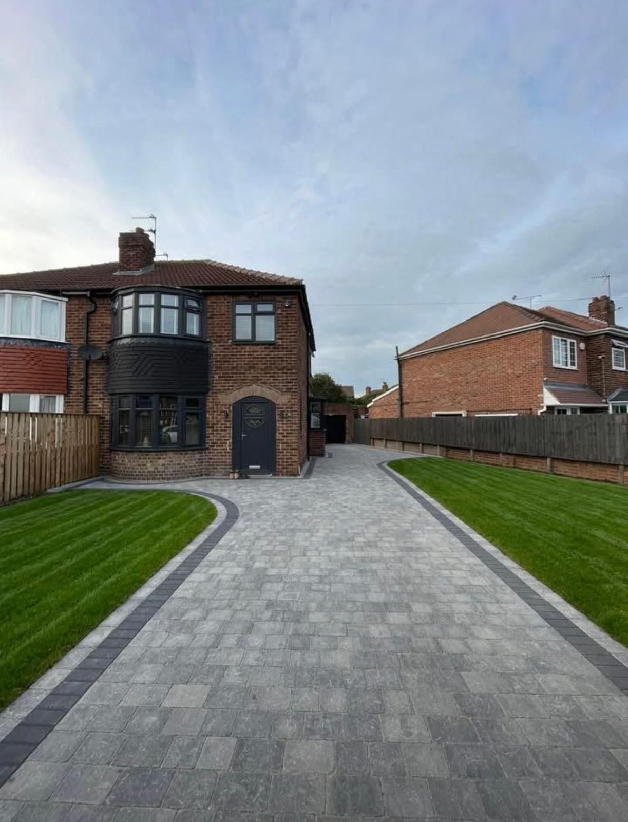 A brick house with a gray paved driveway and green lawn.