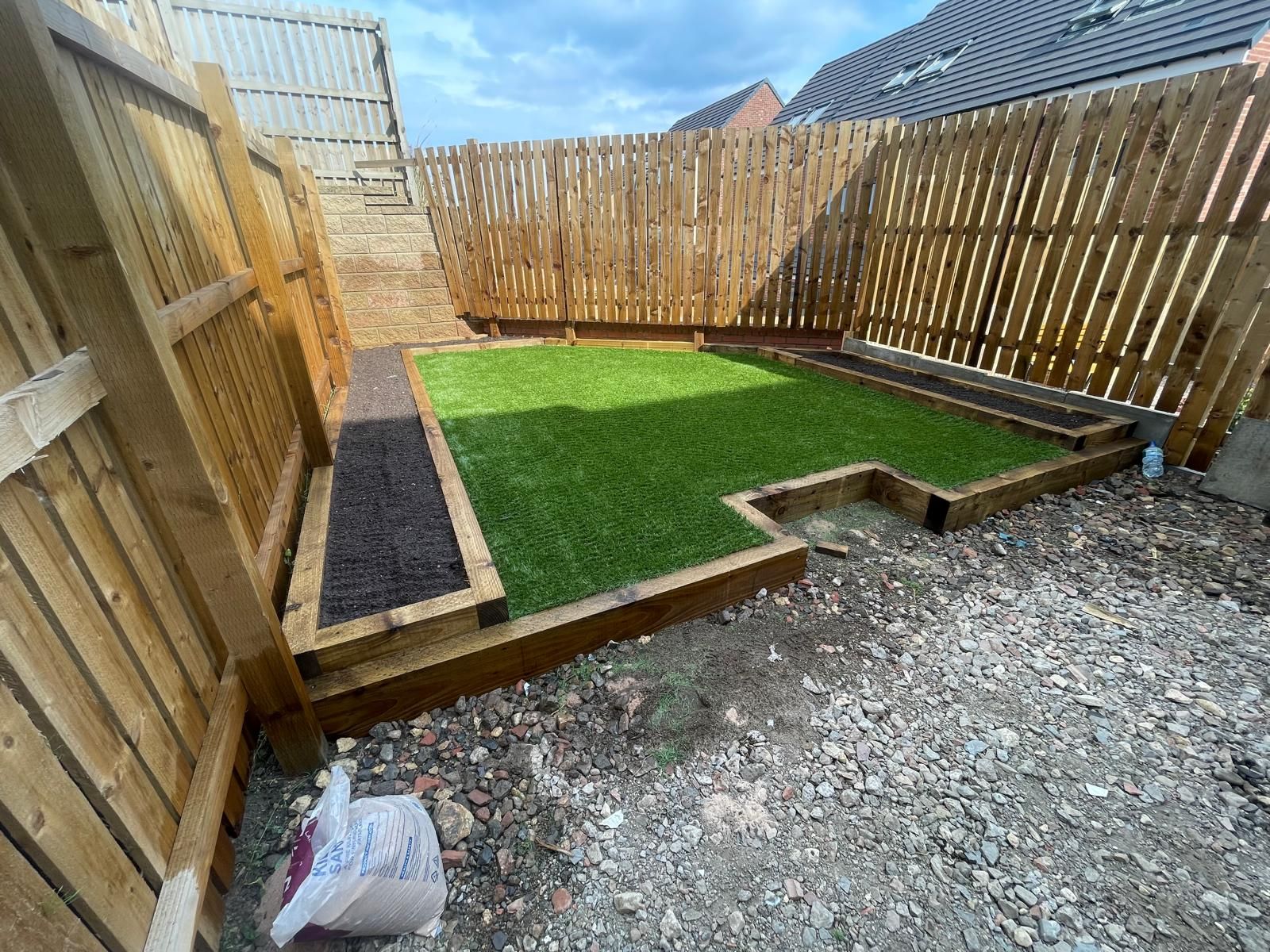 Small backyard with wooden fences, artificial grass, and gravel.