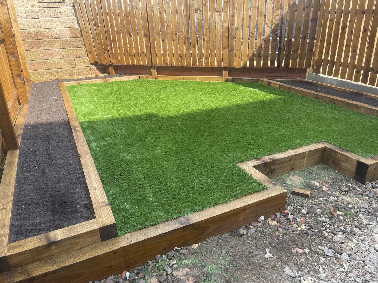 A small, enclosed backyard with green artificial turf surrounded by wooden borders and a wooden fence.