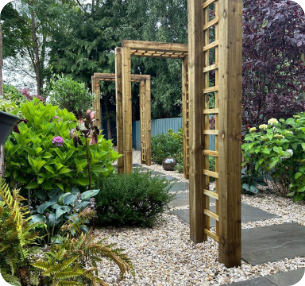 Wooden garden archways over a gravel pathway, surrounded by greenery and plants.