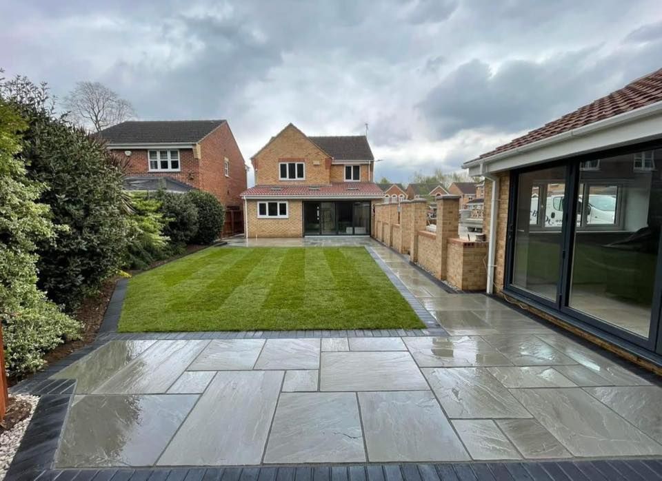 Backyard patio with lawn, brick fence, and house with large glass doors. Overcast sky.