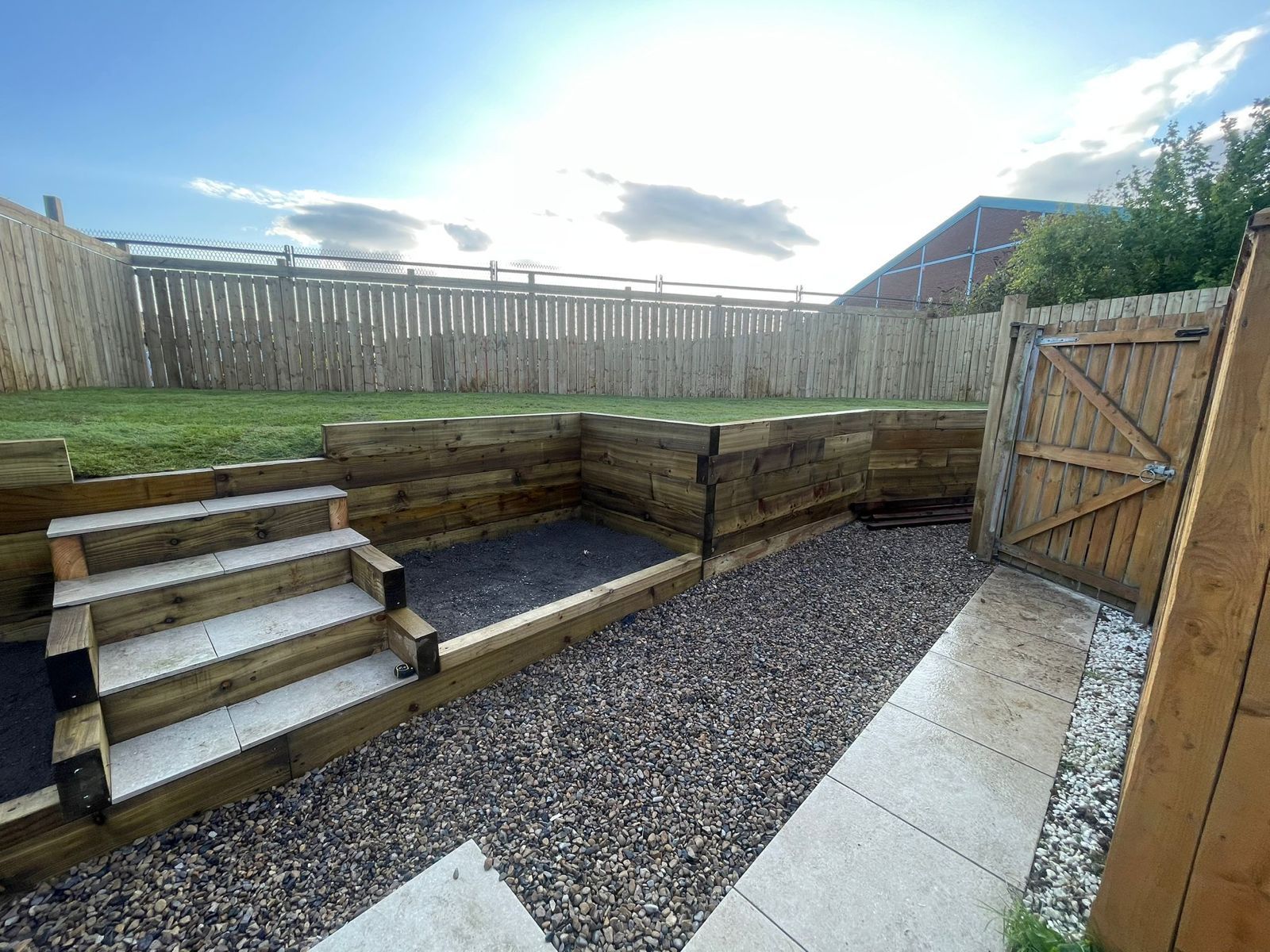 Backyard with tiered wooden seating, gravel floor, and steps beside a fenced patio area