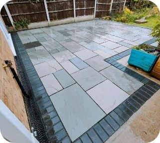 Patio paved with light gray rectangular and square stones, bordered with dark gray bricks.