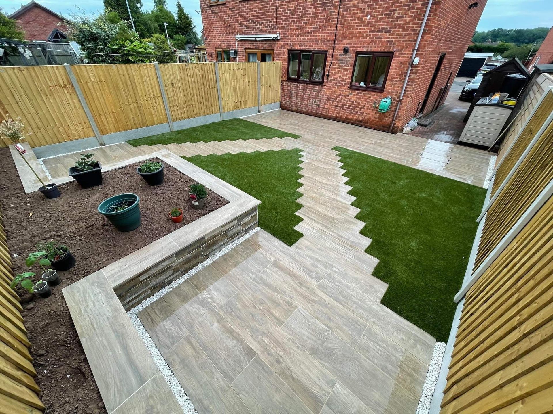A newly landscaped backyard with tiled patio, artificial turf, gravel pathways, and brick house.