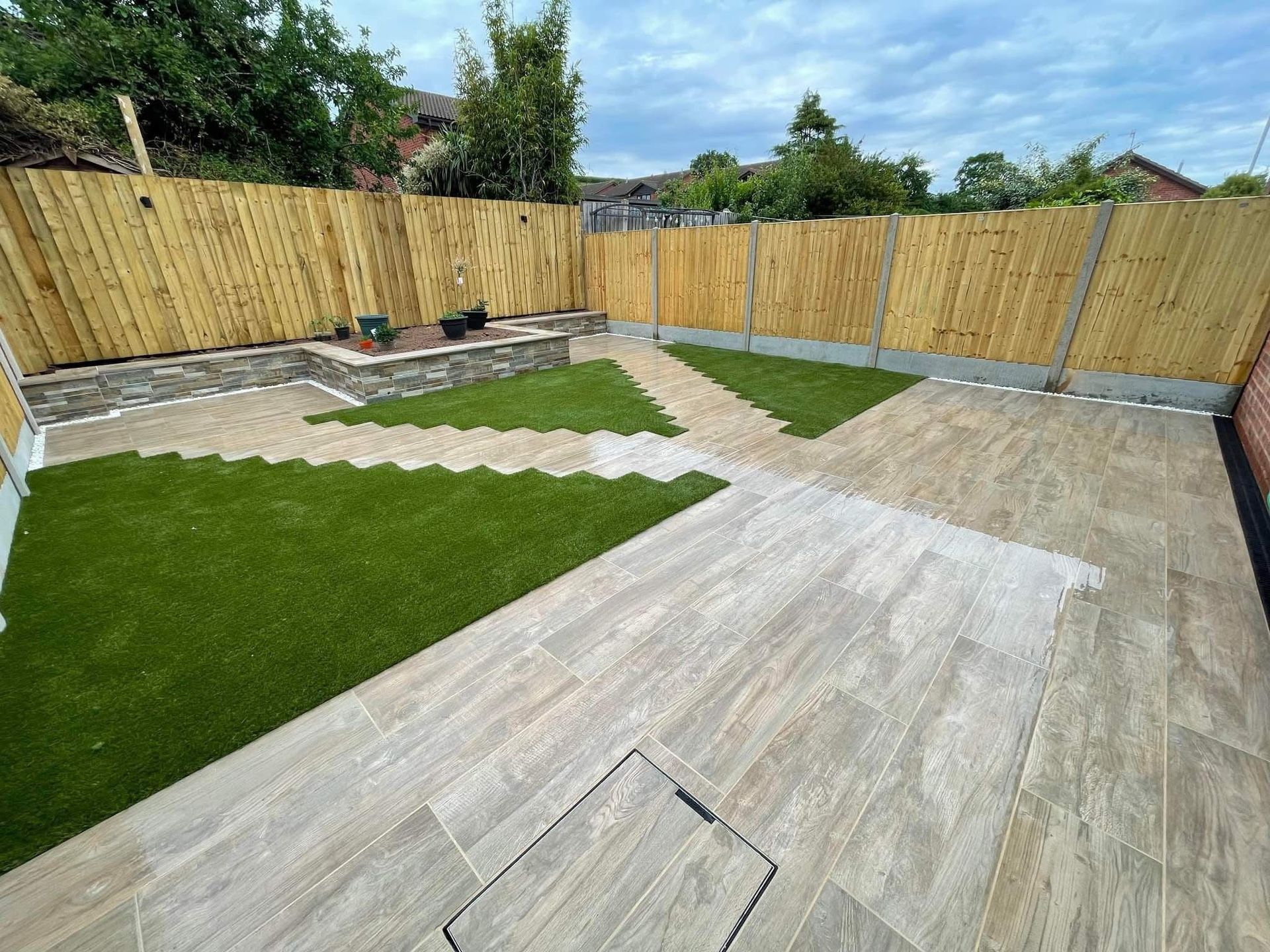 Backyard with beige patio, green turf, and wooden fence.