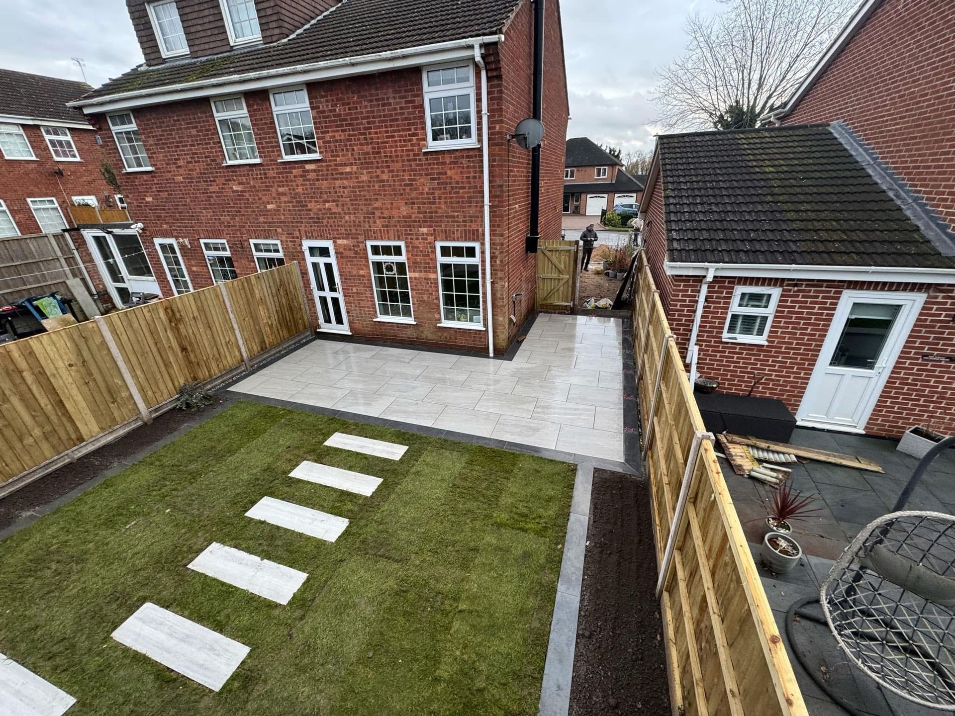 Backyard with lawn, patio, and stepping stones leading to a red brick house and a small building with a white door.