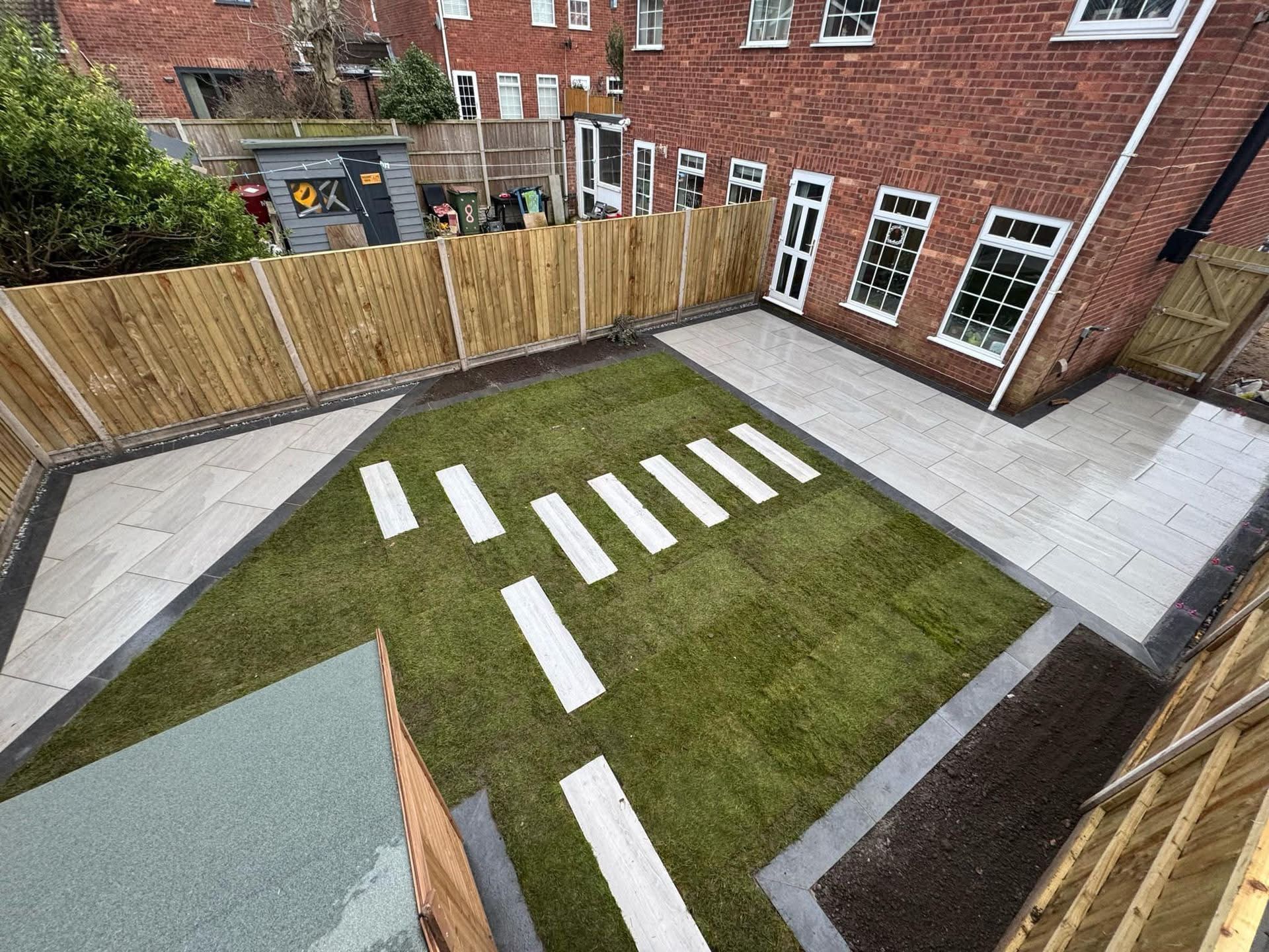 Backyard with green lawn, stone path, wooden fence, and brick house.