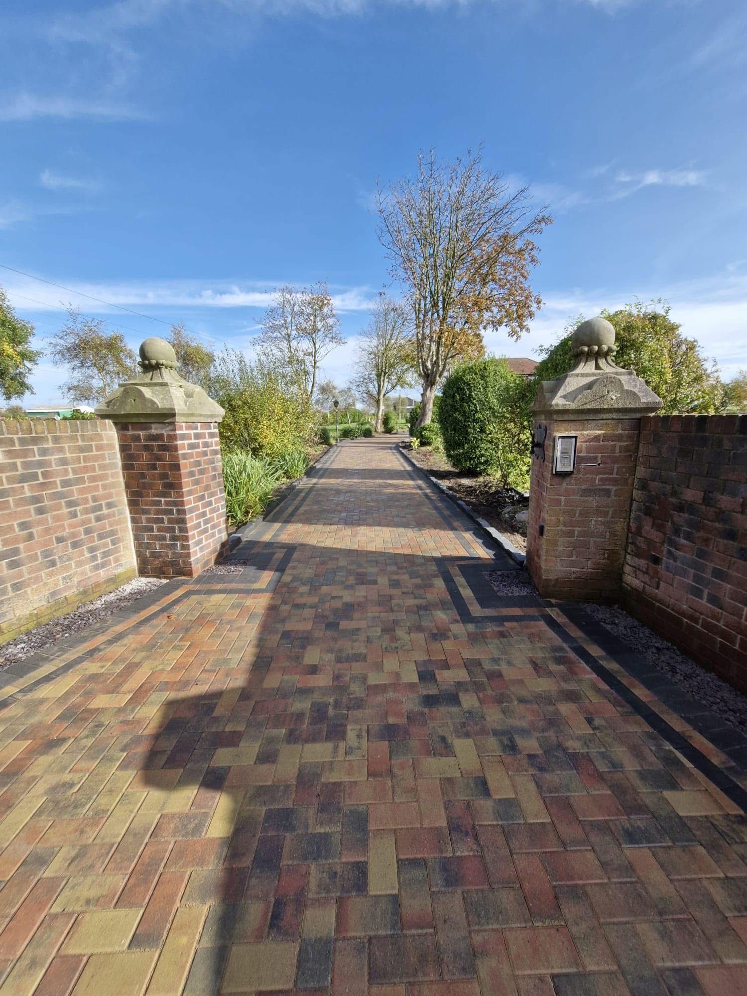Brick paved walkway with brick pillars under a blue sky.