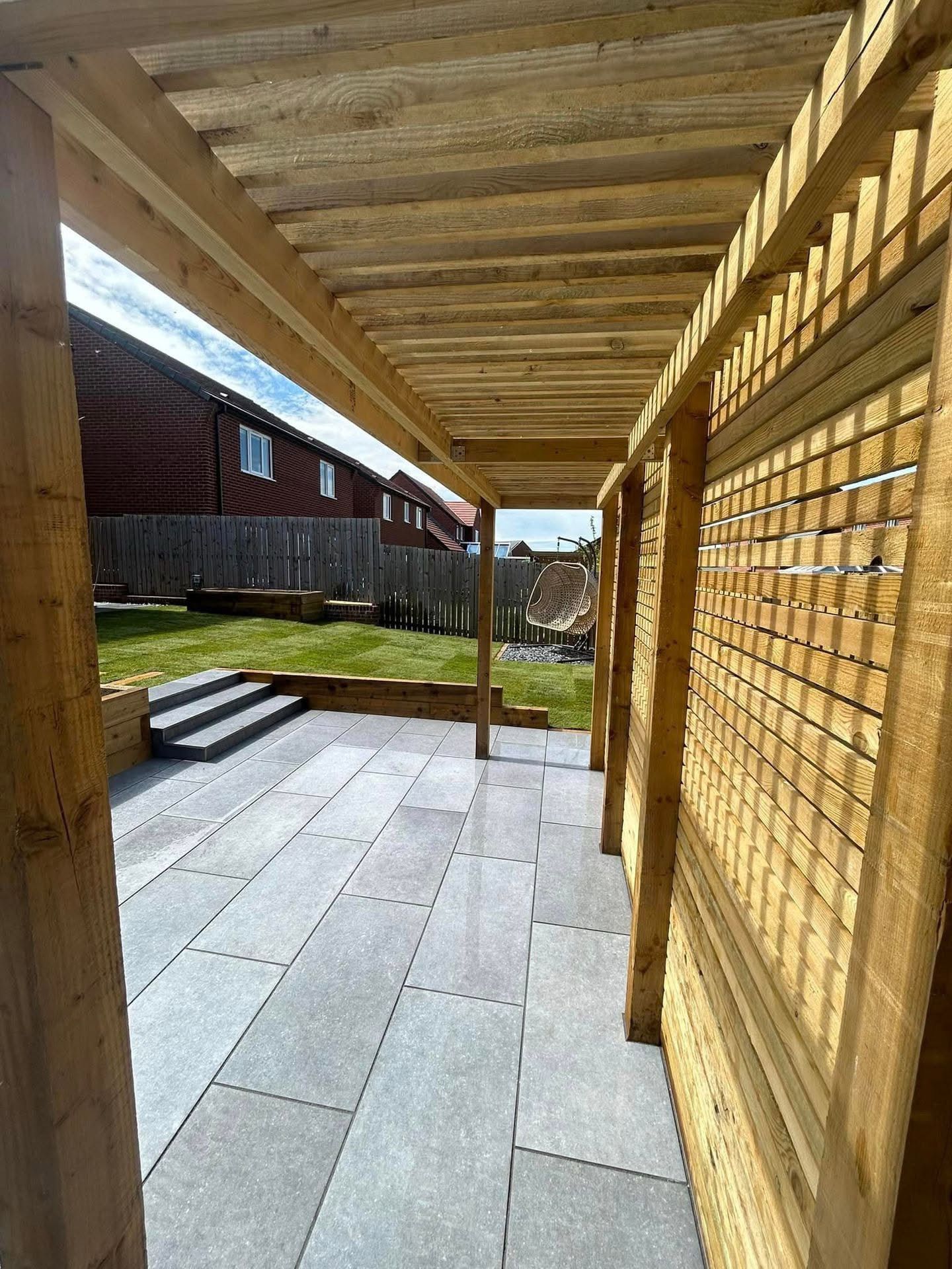 Patio with gray stone tiles, wooden pergola, and lattice side panel.