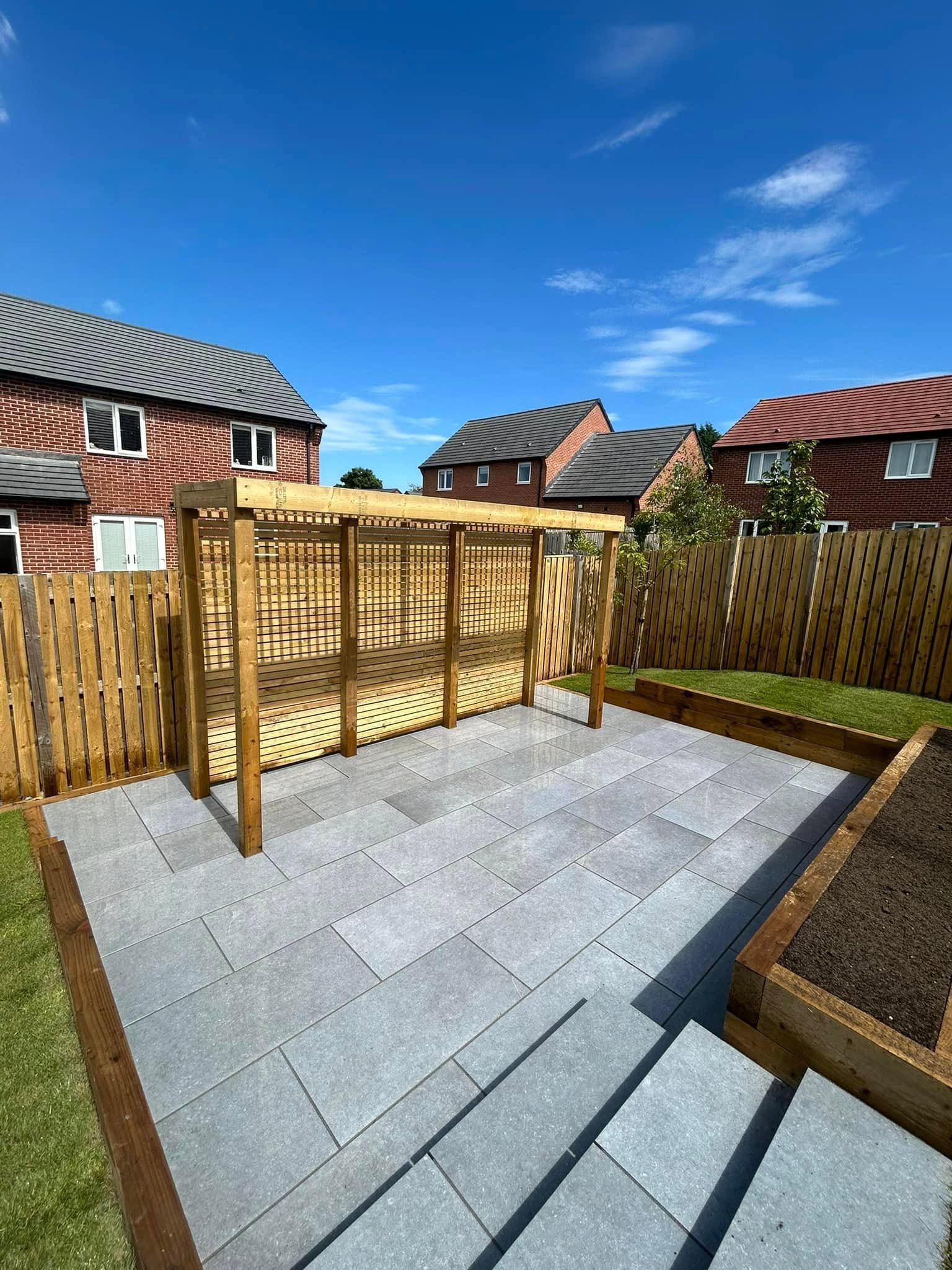 Patio with a wooden pergola, surrounded by a wooden fence, and green grass on a sunny day.