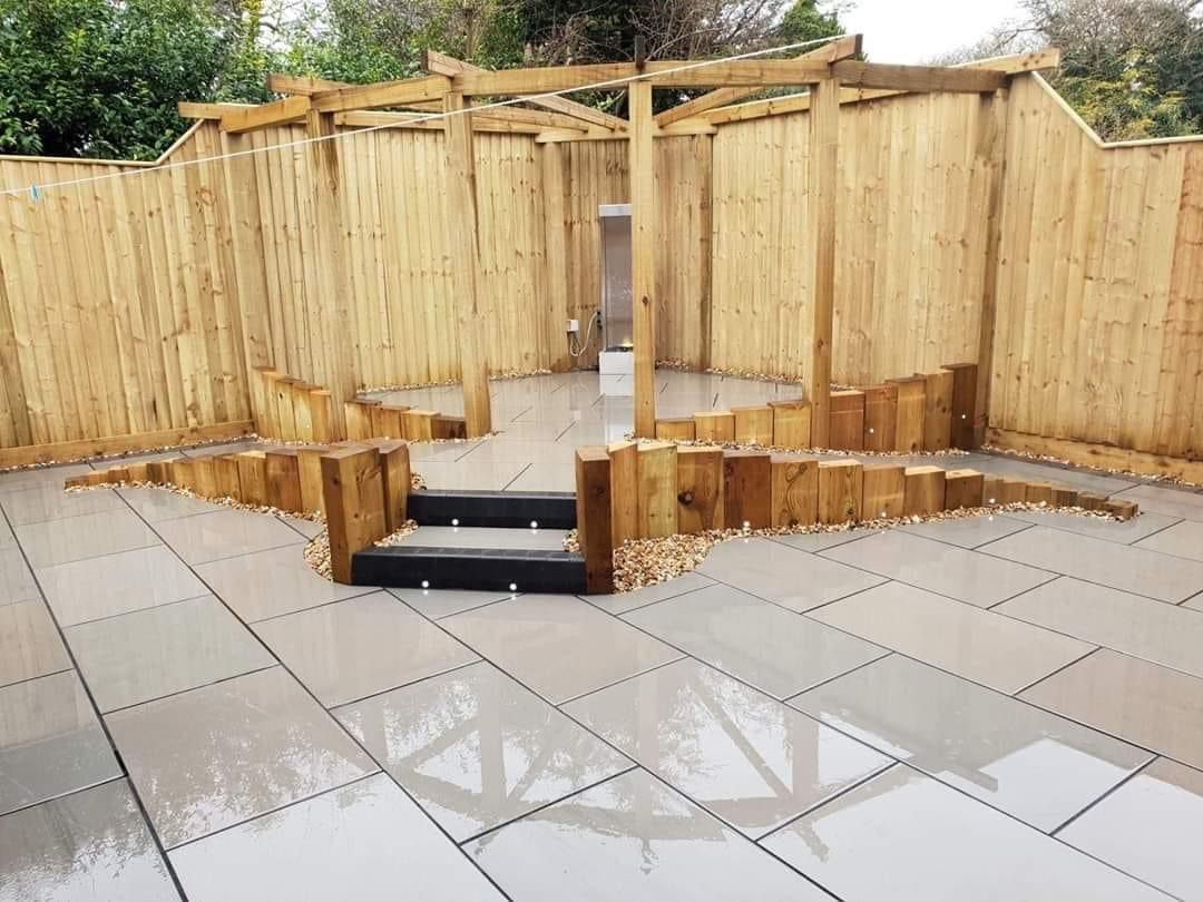 Wooden gazebo with a stone patio and wooden fence.
