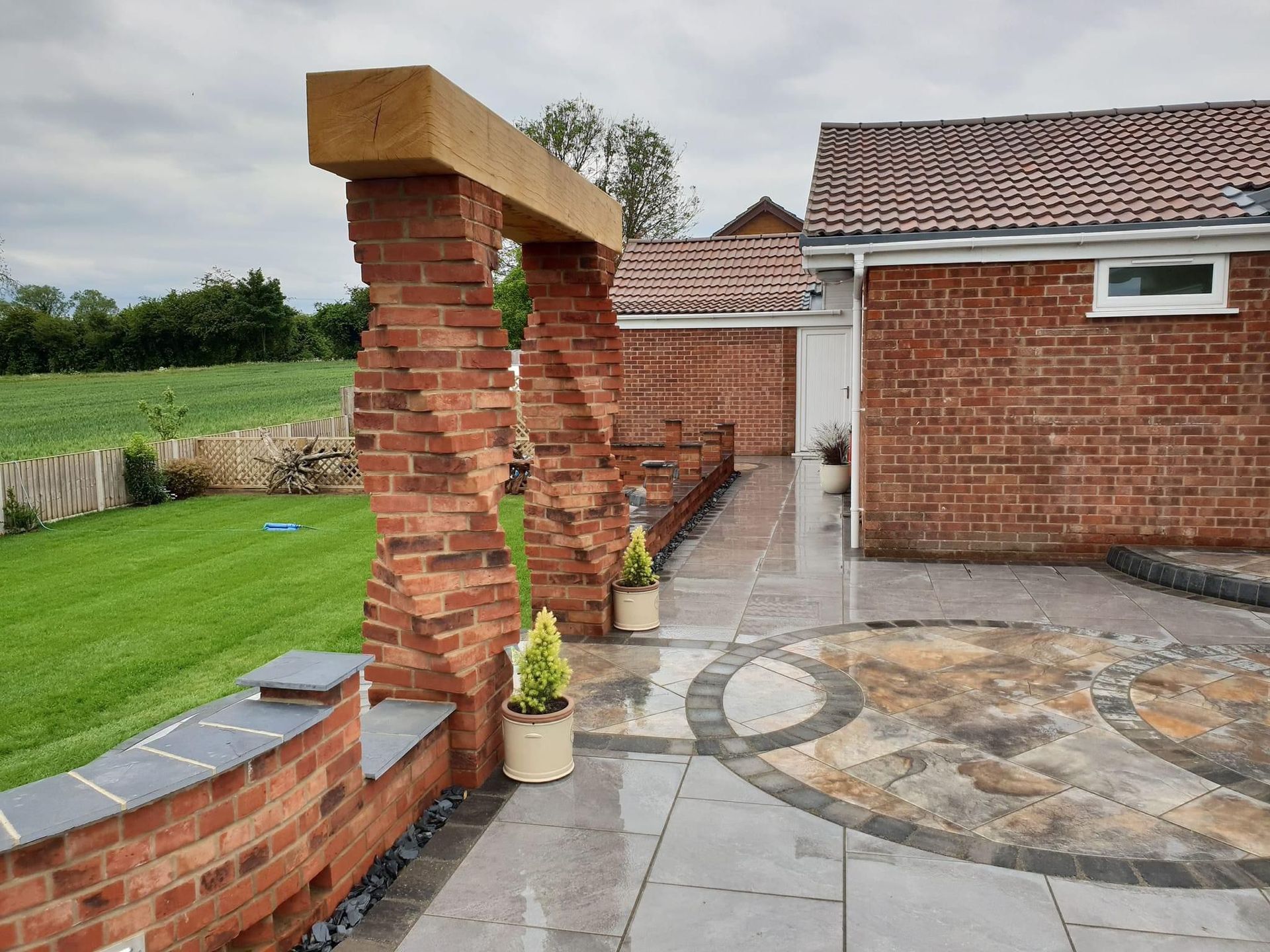 Brick patio with spiral brick columns and rectangular yellow beam, adjacent to a grassy lawn and a red brick building.