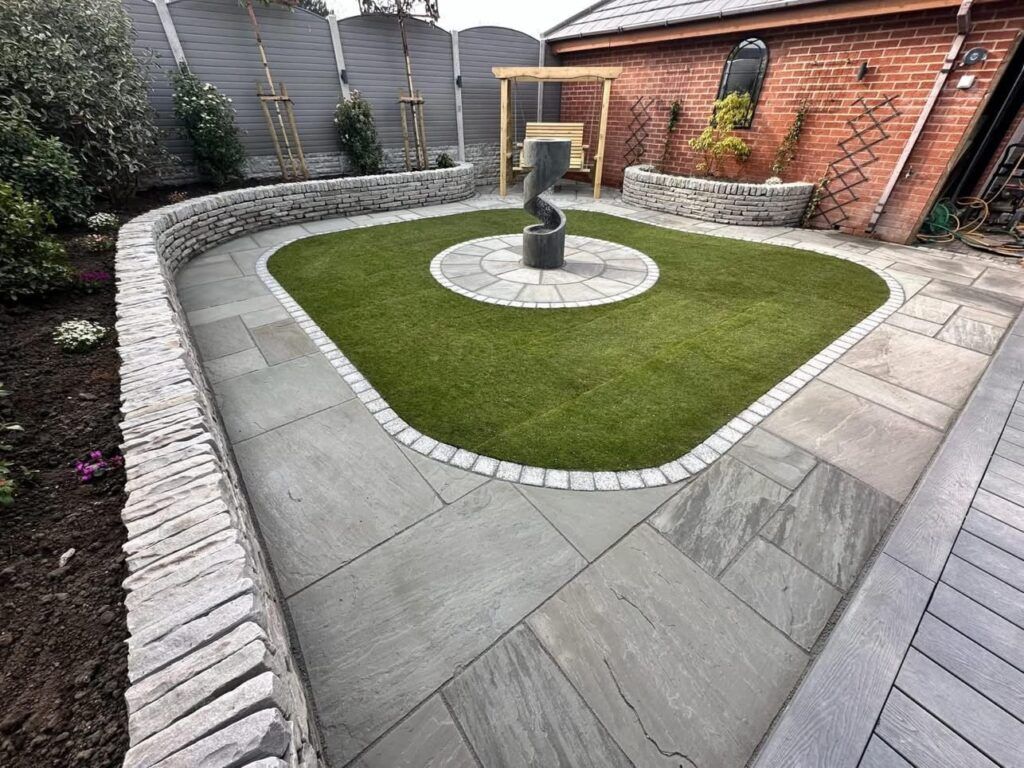 Stone patio with curved brick wall and green lawn, sculpture focal point.