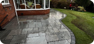 Wet stone patio next to green lawn and a brick building with a glass conservatory.