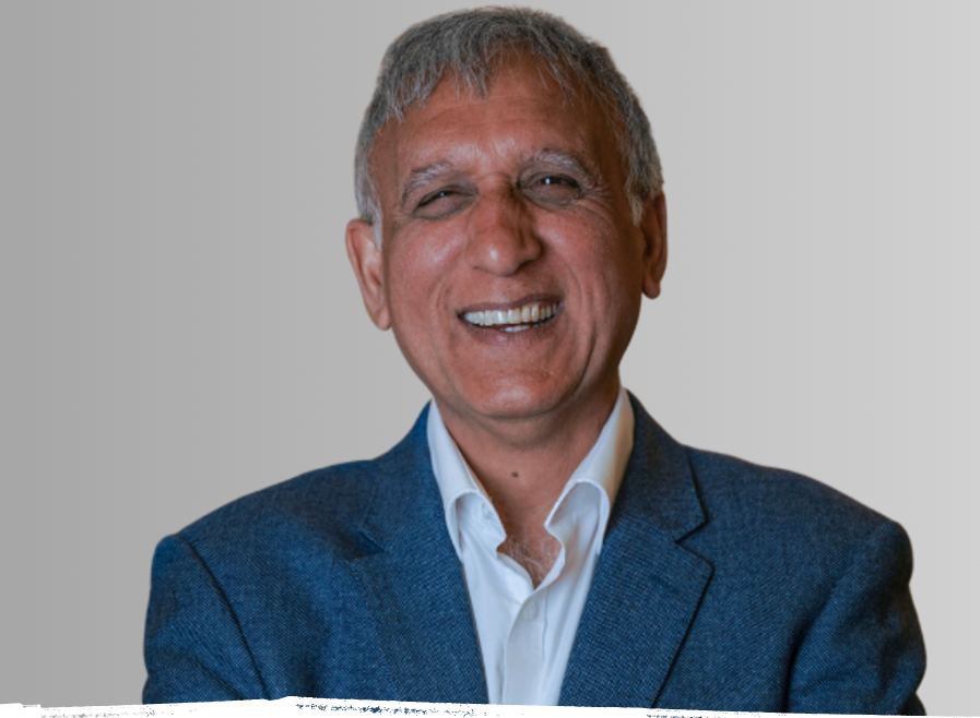 Smiling man in a blue blazer and white shirt, against a gradient gray backdrop.