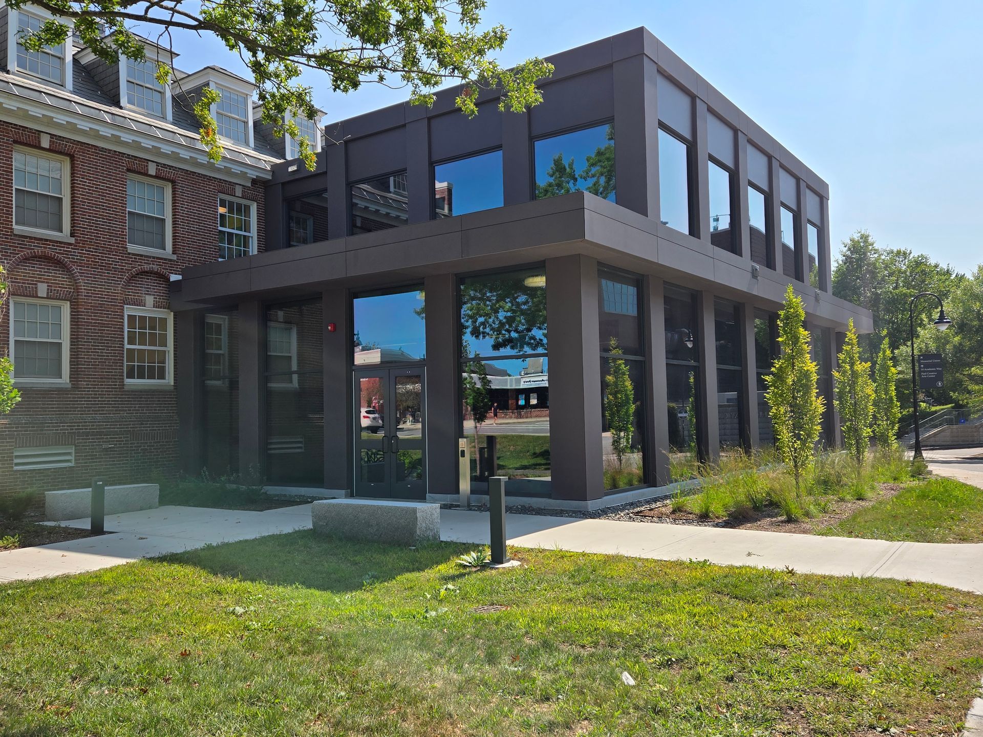 Modern building with large windows, adjacent to a brick building. Exterior shot on a sunny day.