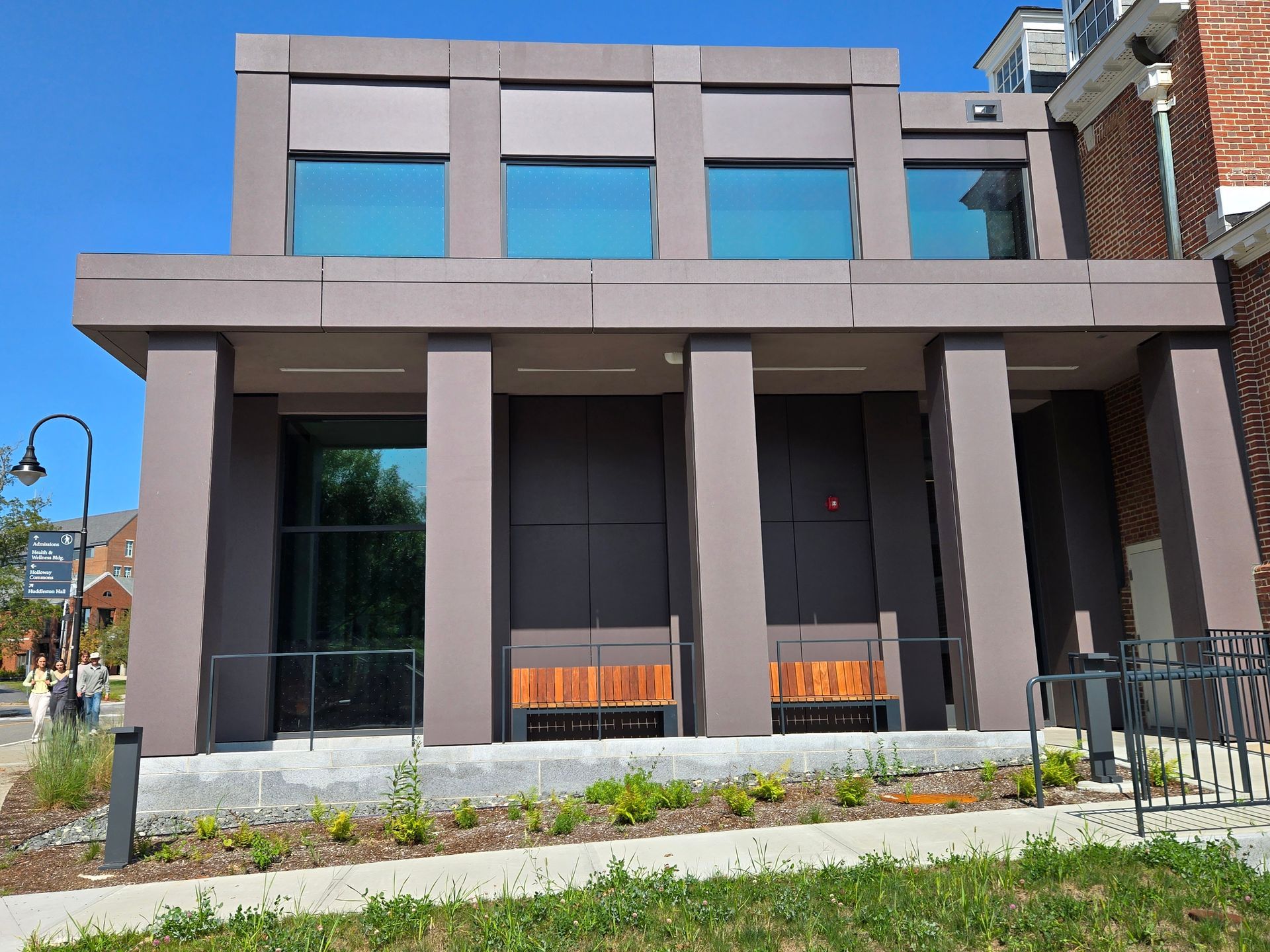 Modern building with brown columns, teal windows, and wooden benches.