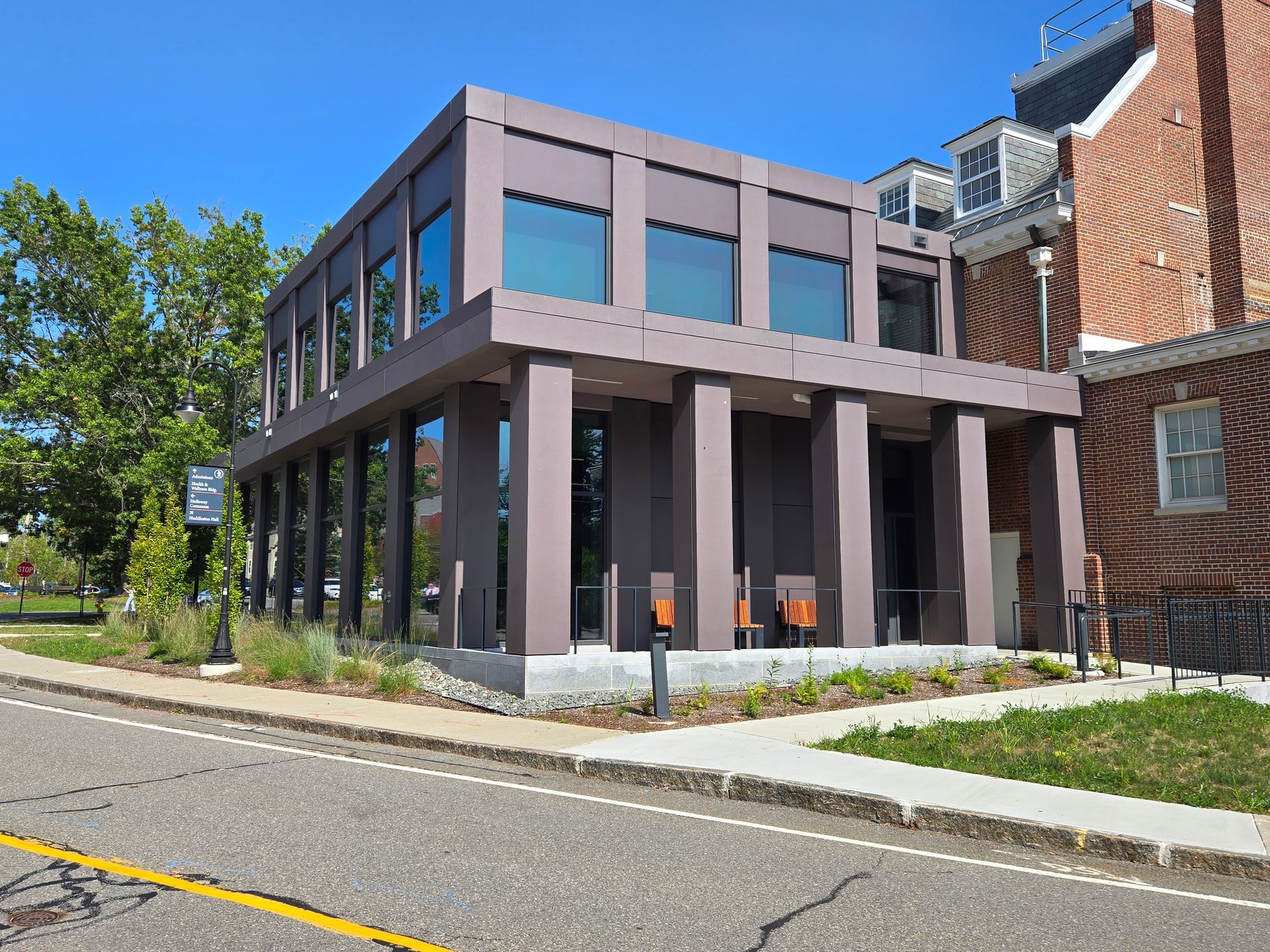 Modern building with large windows and columns; adjacent to a brick building on a sunny day.