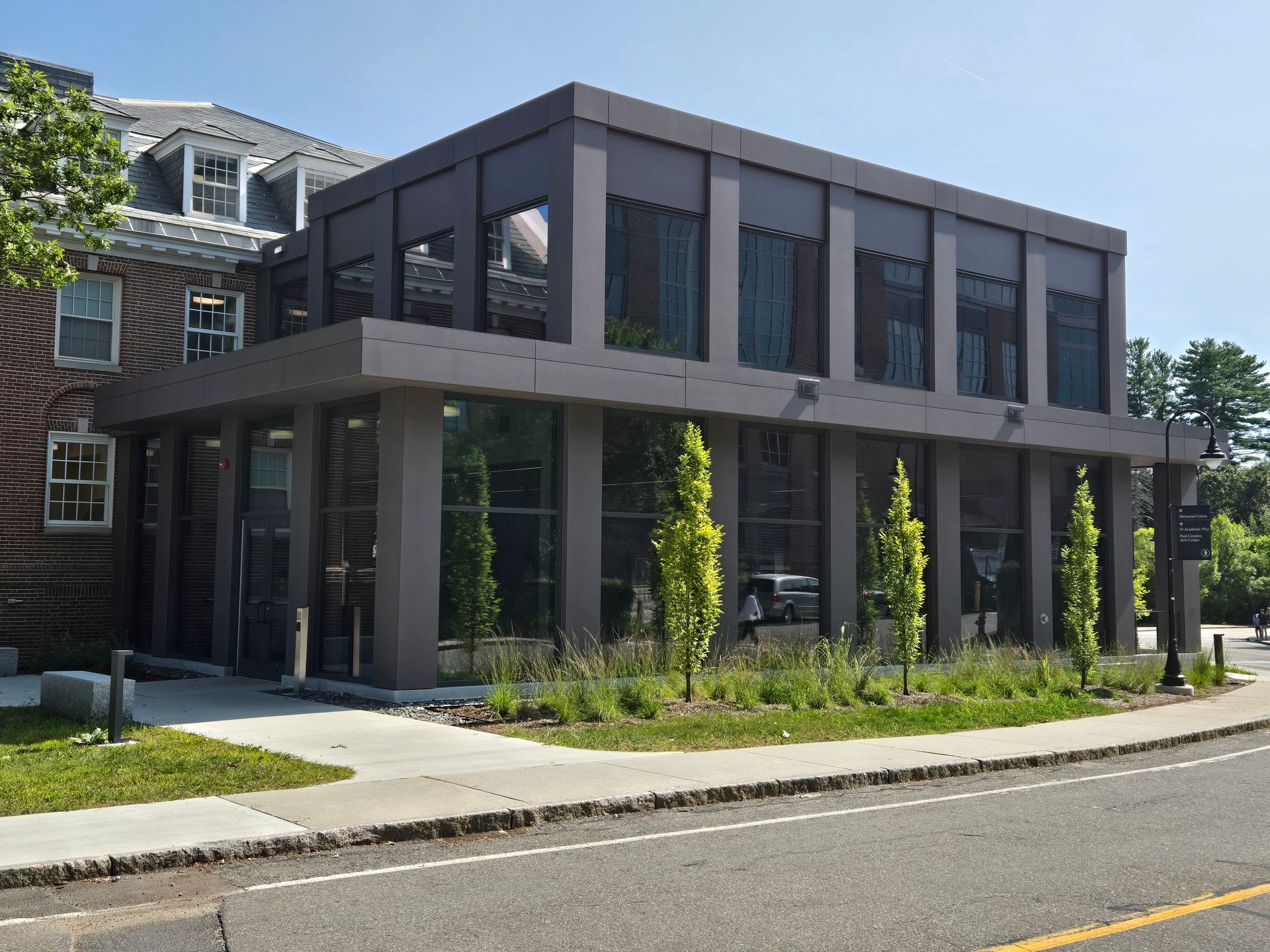 Modern two-story building with dark gray exterior and large windows, adjacent to a brick building.