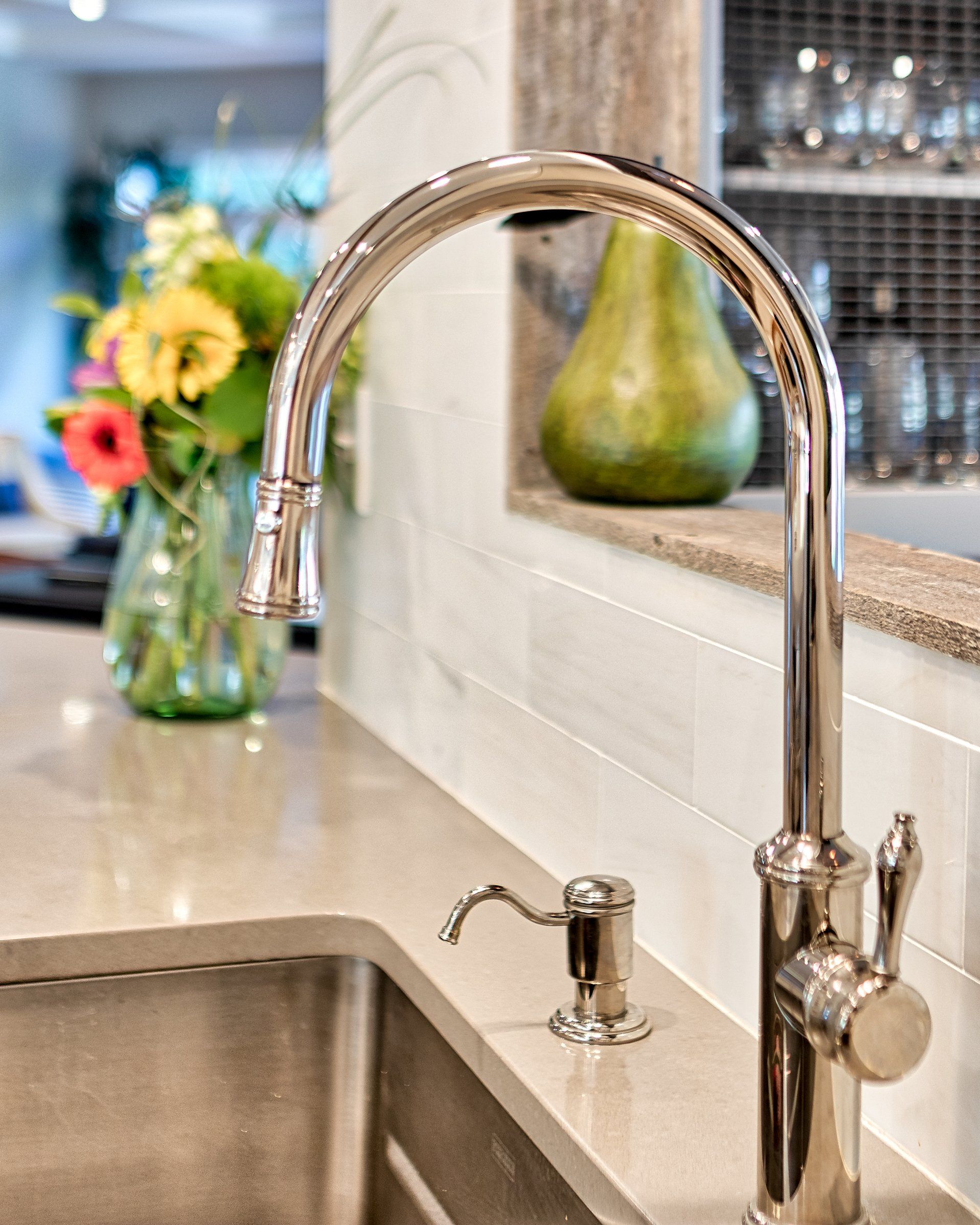 A kitchen sink with a faucet and a vase of flowers in the background