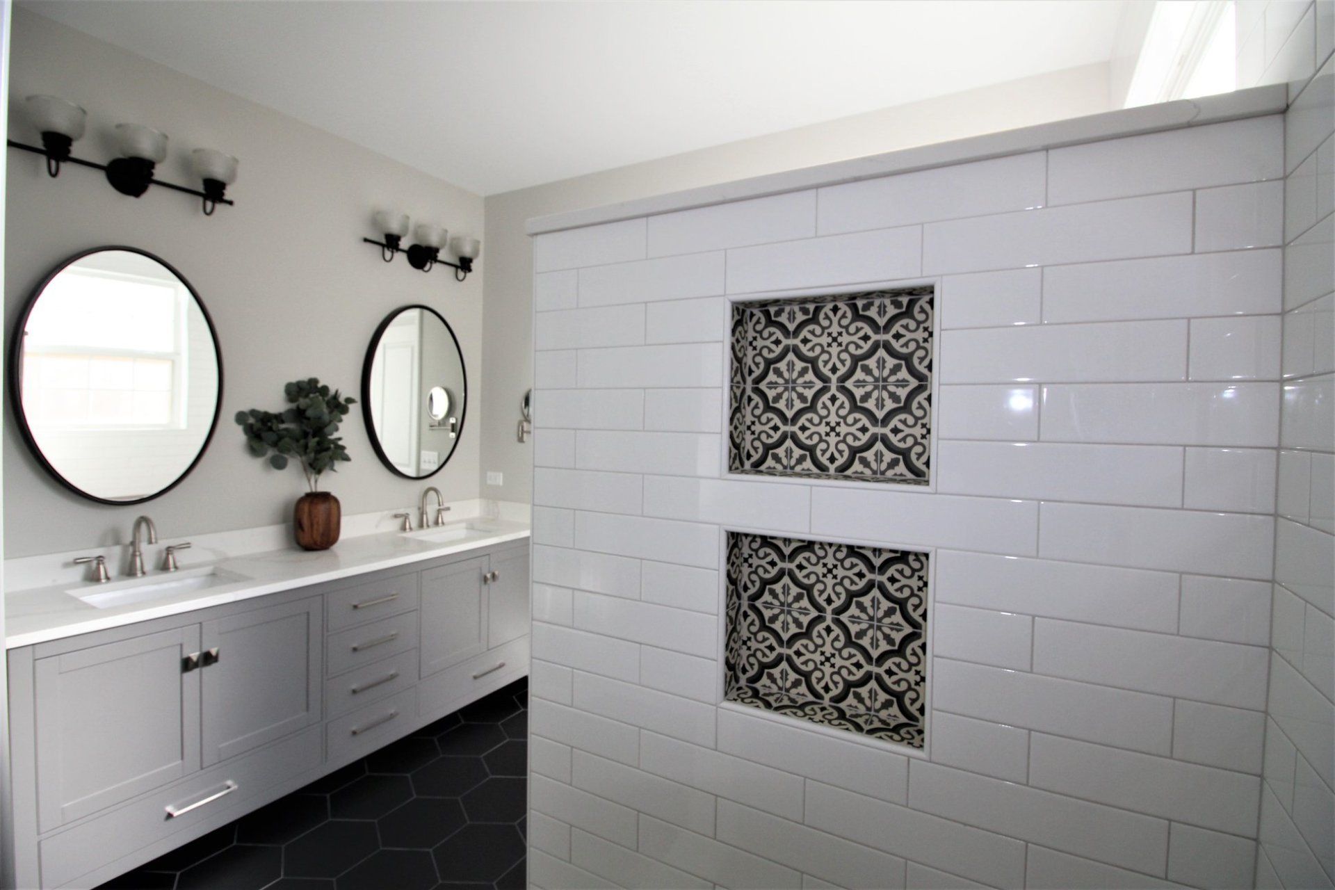 A bathroom with two sinks , two mirrors , and a walk in shower.