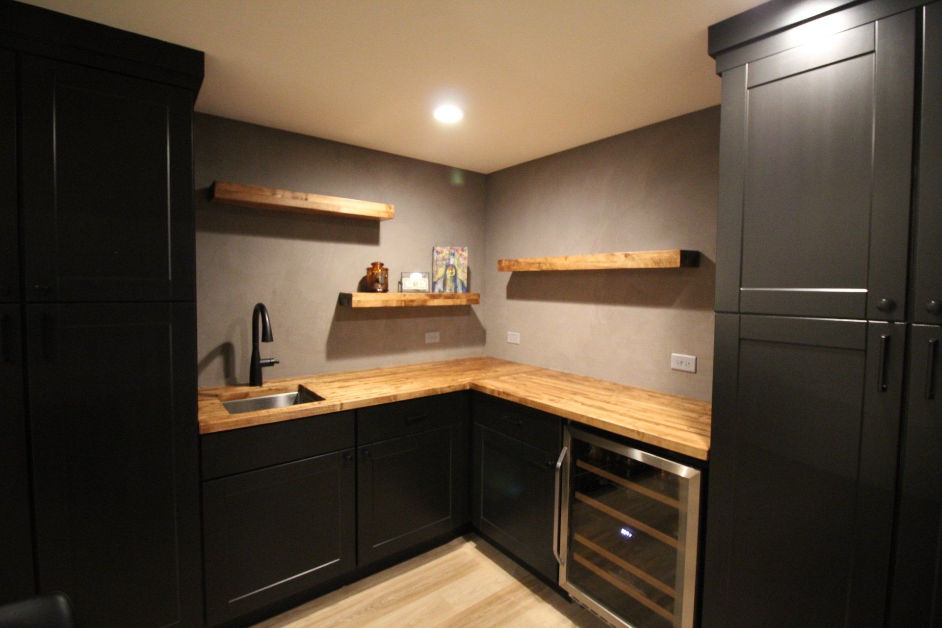 A kitchen with black cabinets , wooden counter tops , a sink and a wine cooler.