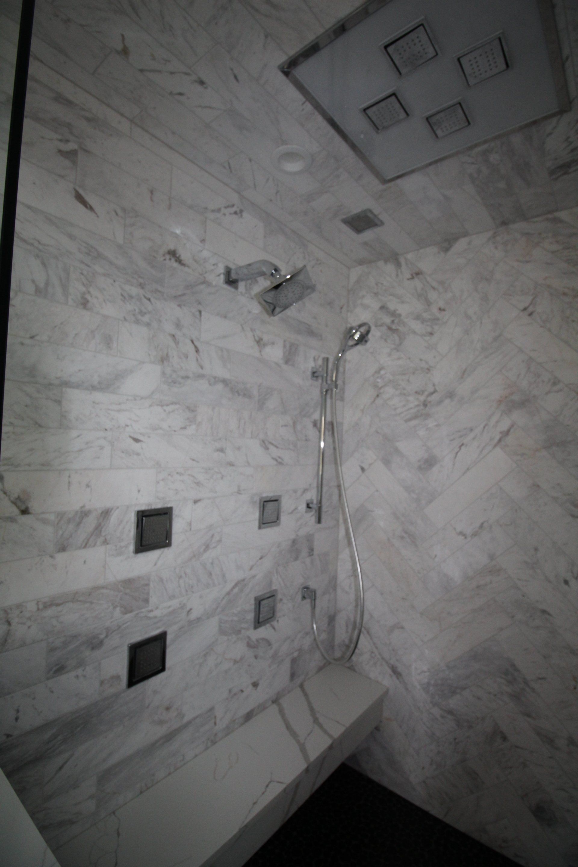 A shower with a bench and a shower head on the wall.