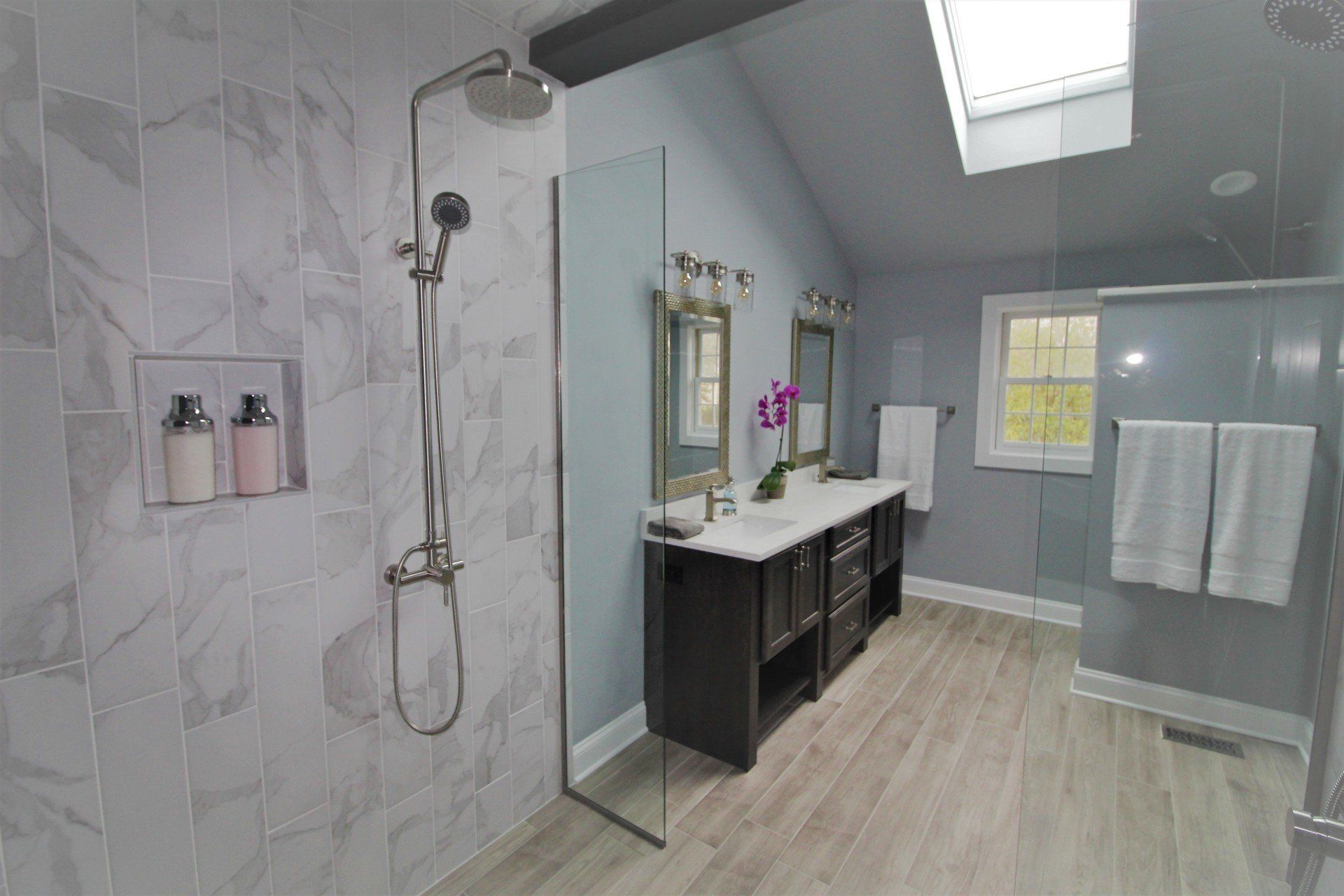 A bathroom with two sinks , a walk in shower and a skylight.
