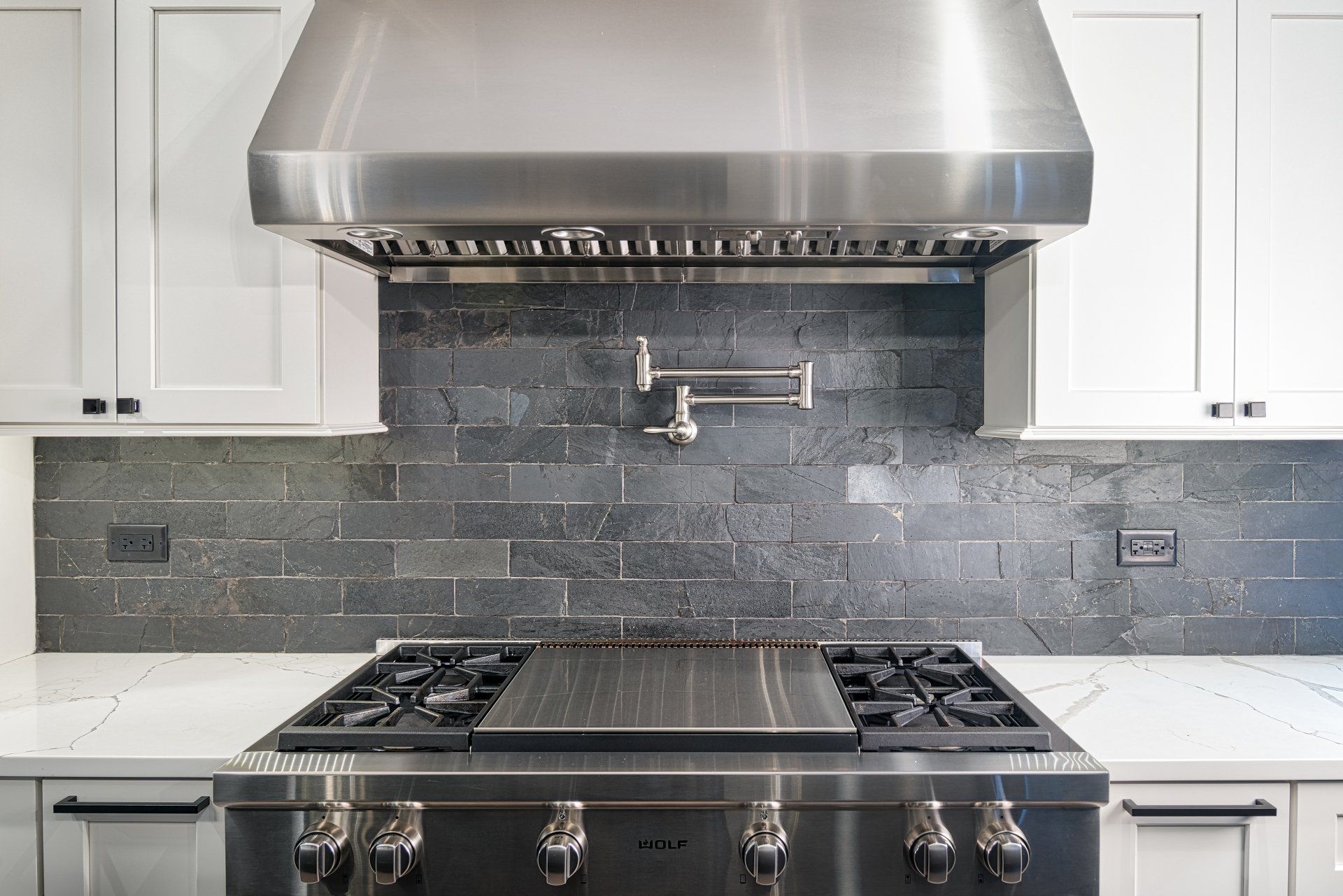 A stainless steel stove top oven with a hood above it in a kitchen.