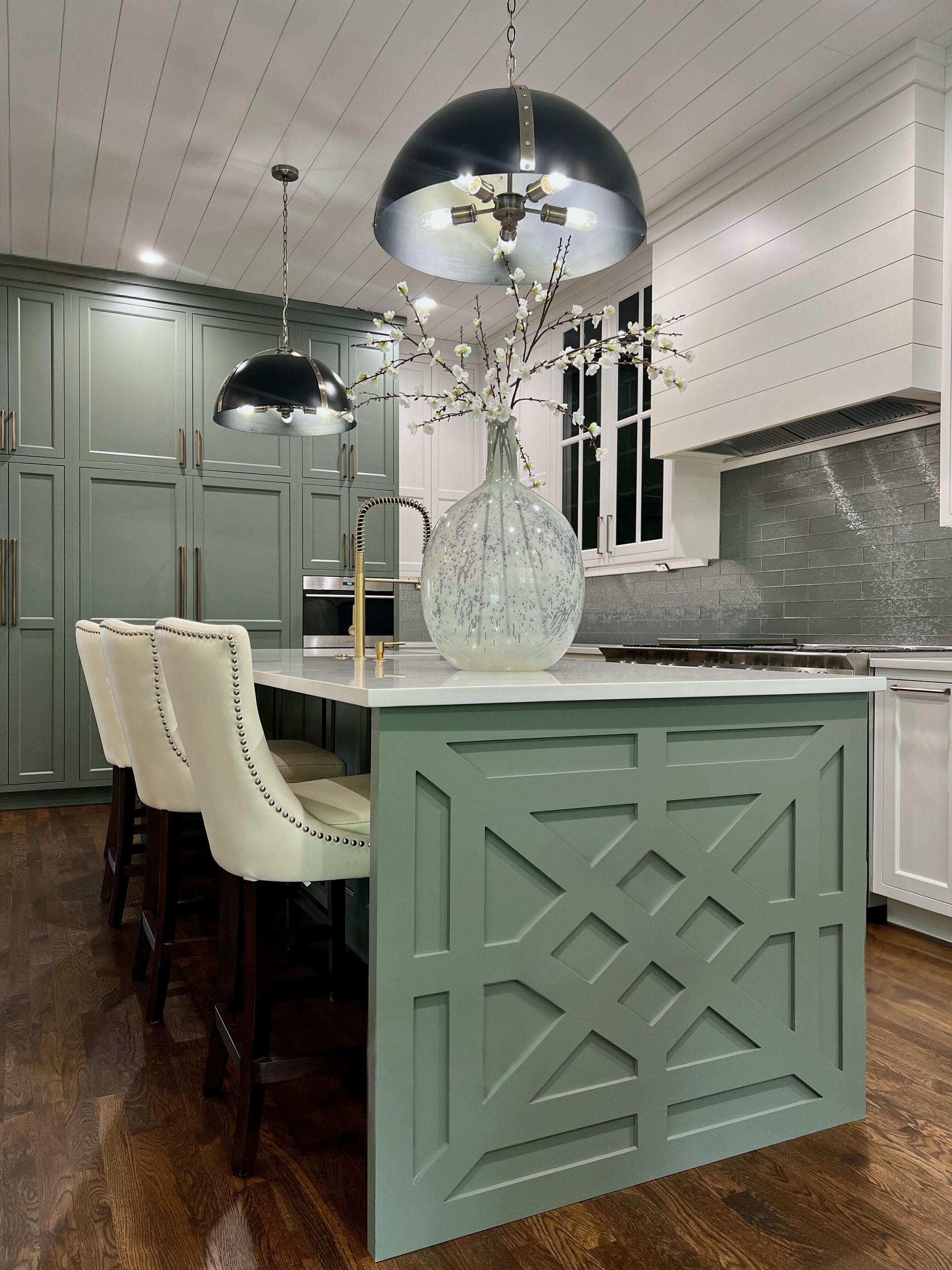 A kitchen with a green island and white chairs