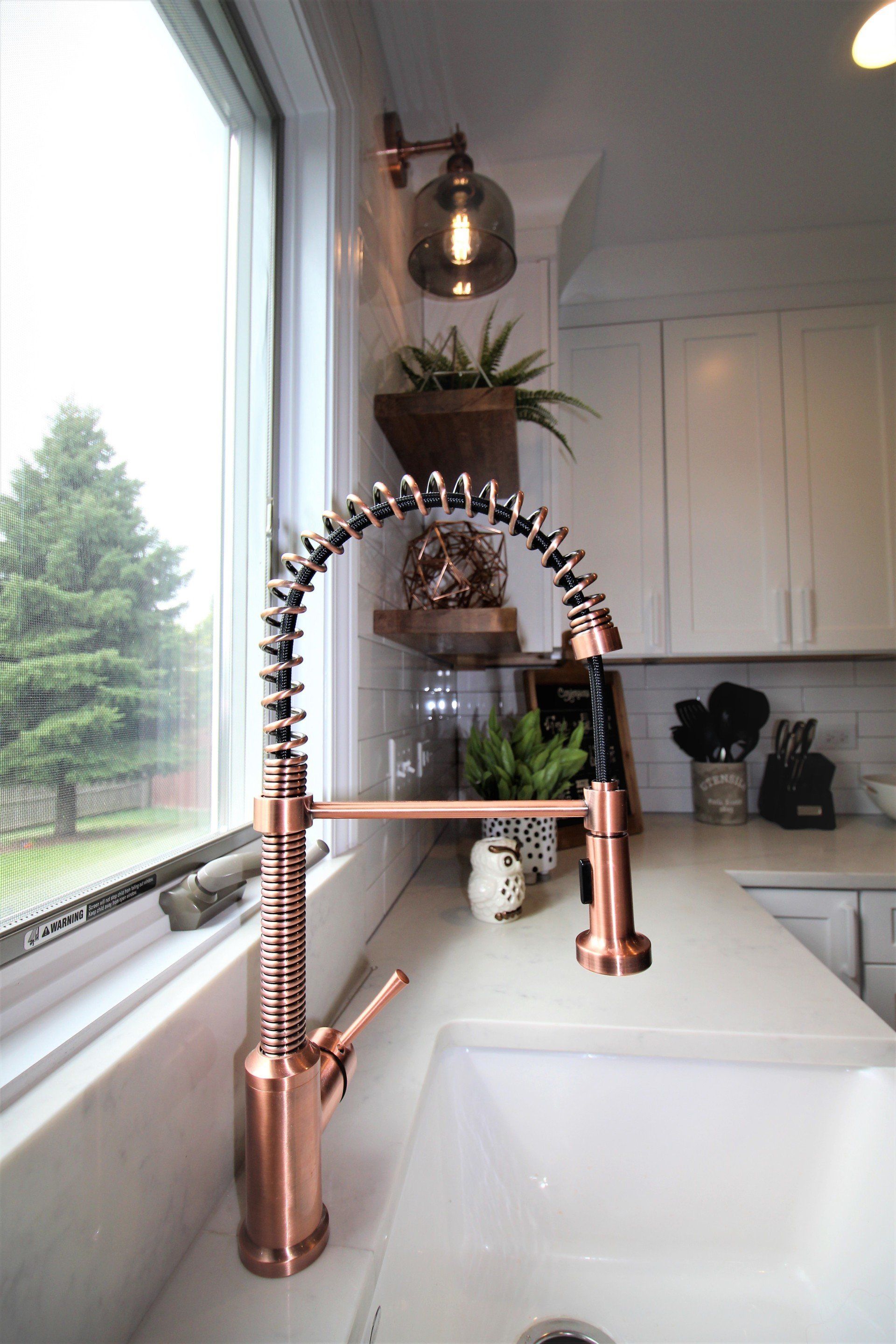 A kitchen sink with a copper faucet next to a window.